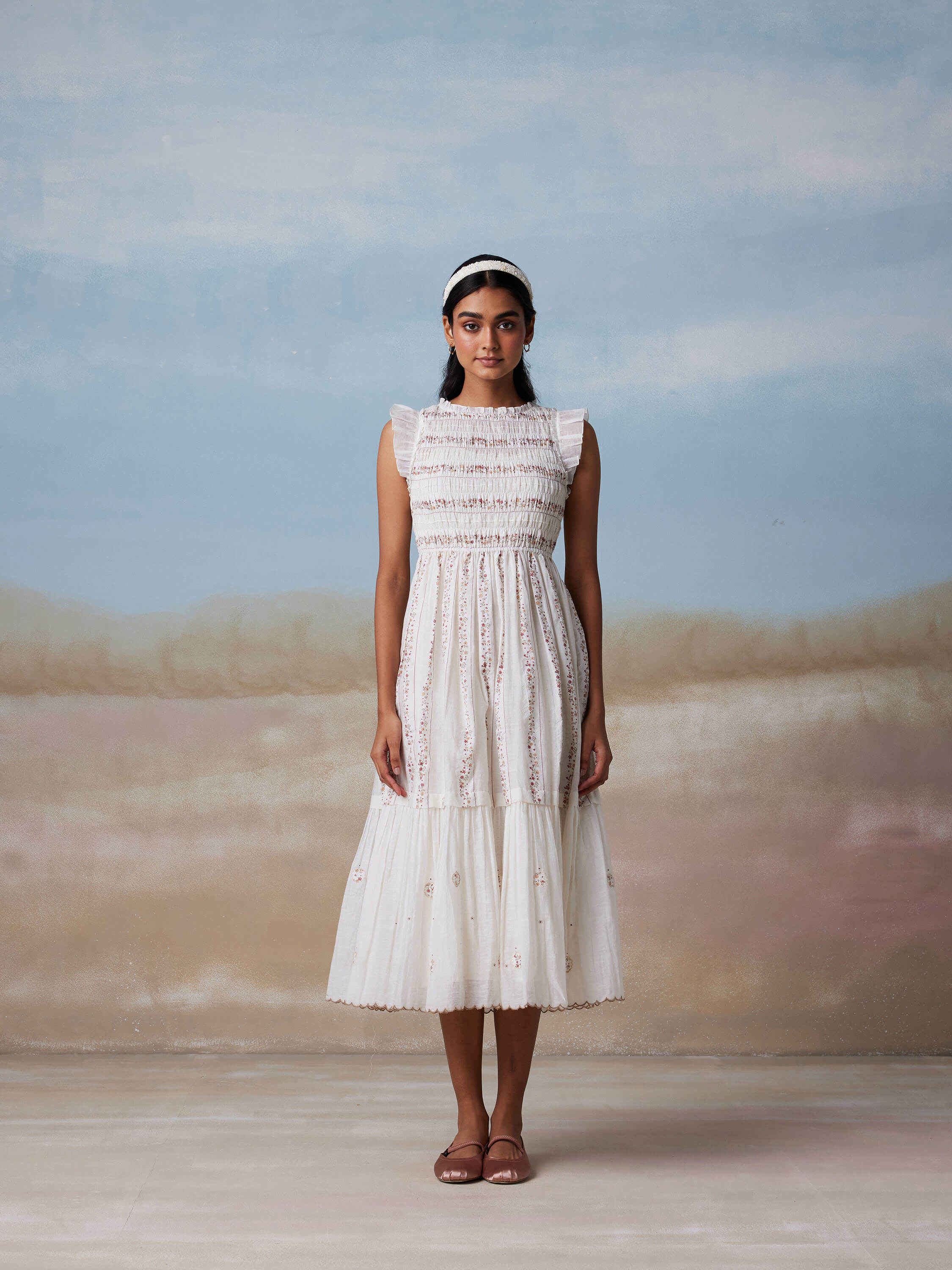 Woman in a white sleeveless dress with pastel background.