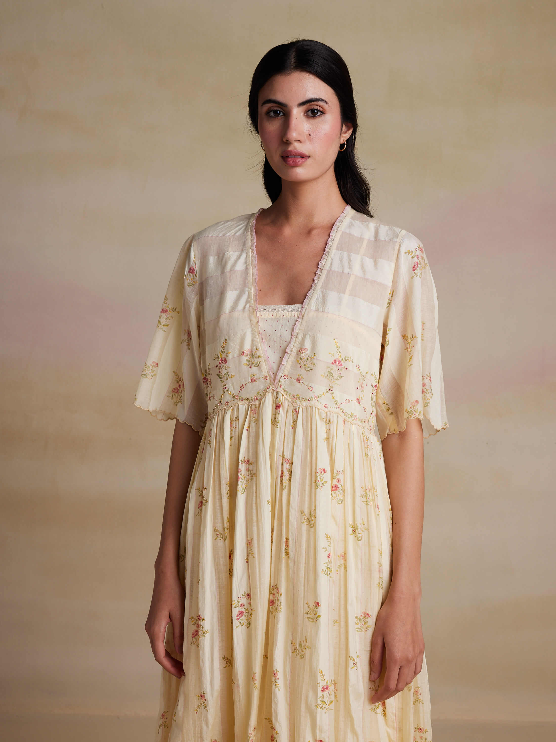 Woman wearing a cream floral dress with soft background.