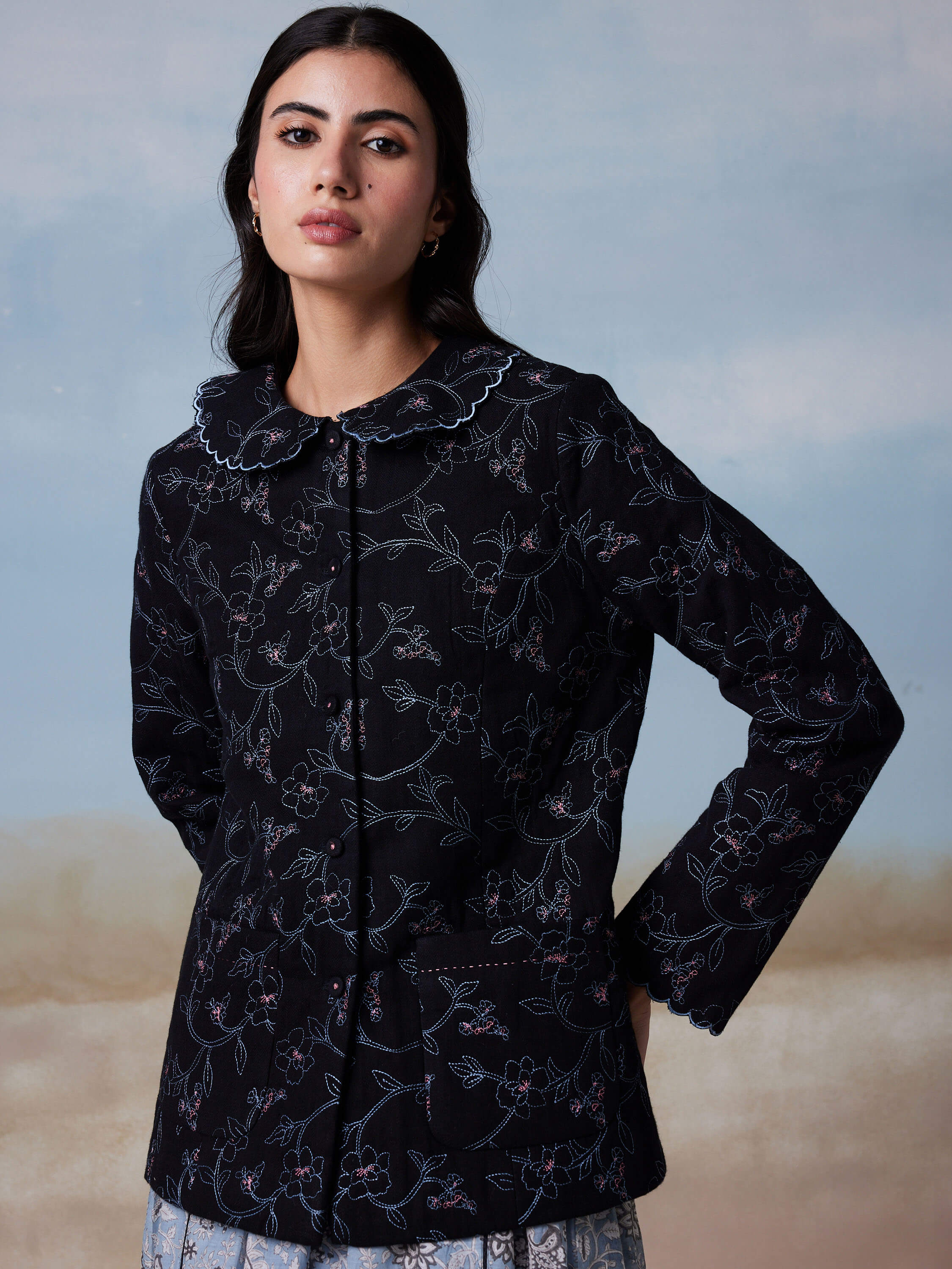 Woman wearing black floral-patterned jacket with scalloped collar.
