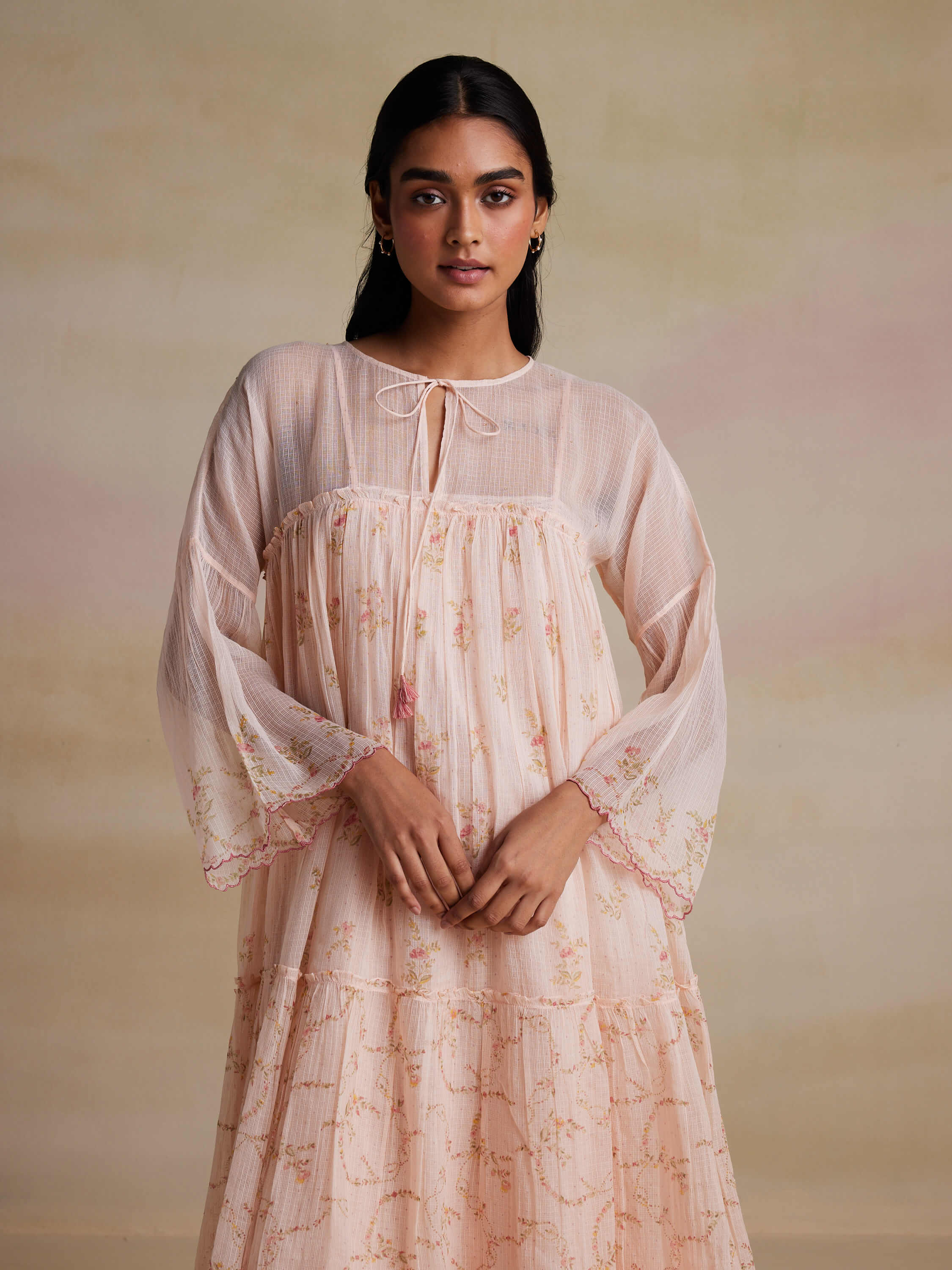 Woman wearing a light pink floral dress with bell sleeves.