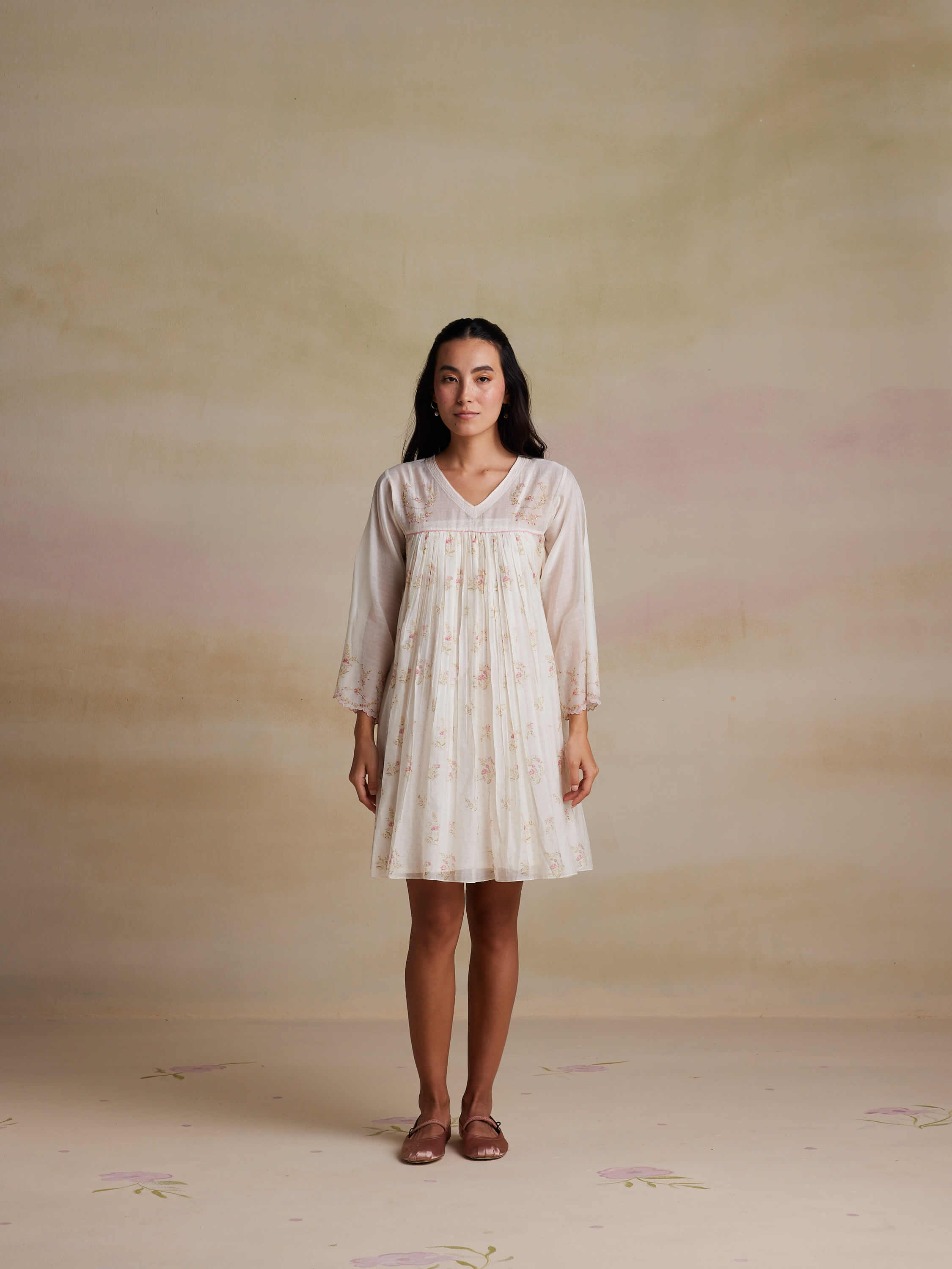 Woman wearing a light floral dress stands against a neutral background.
