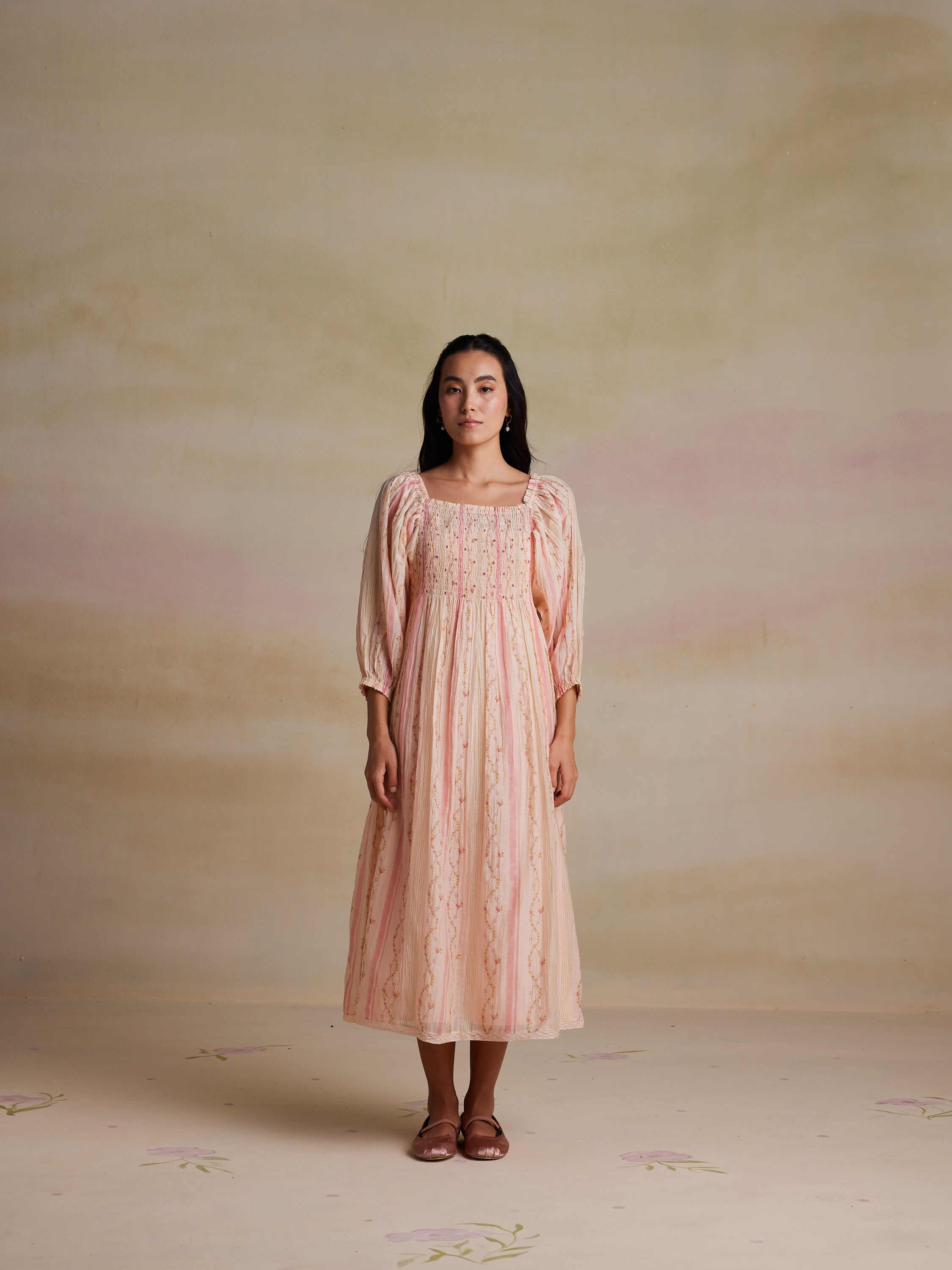 Woman in vintage-style floral pink dress standing on pastel background.