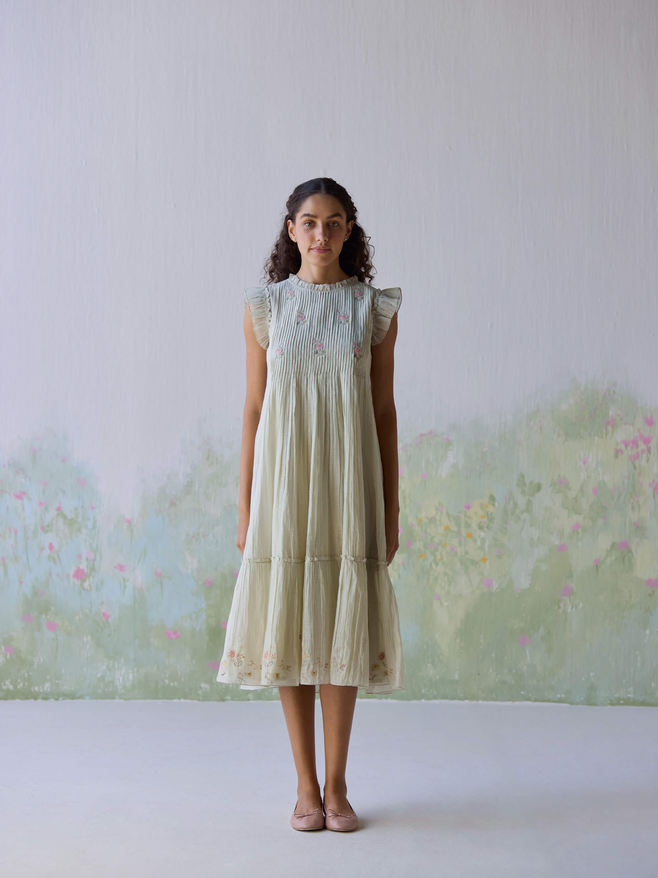 Model wearing Flutter Fields Midi Dress against pastel floral background.