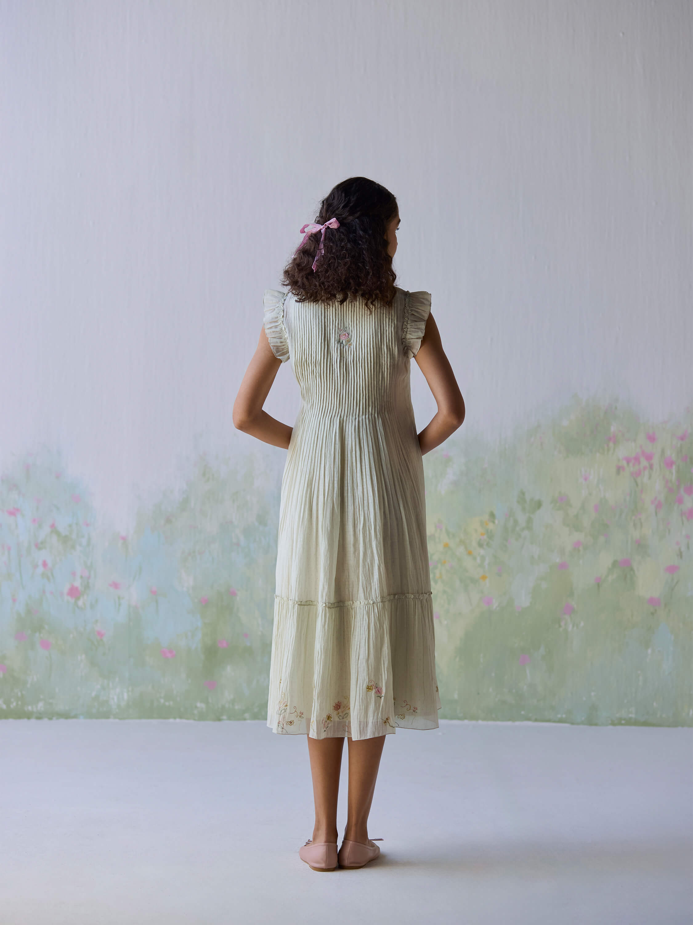 Model wearing Flutter Fields Midi Dress, showcasing back view in floral setting.