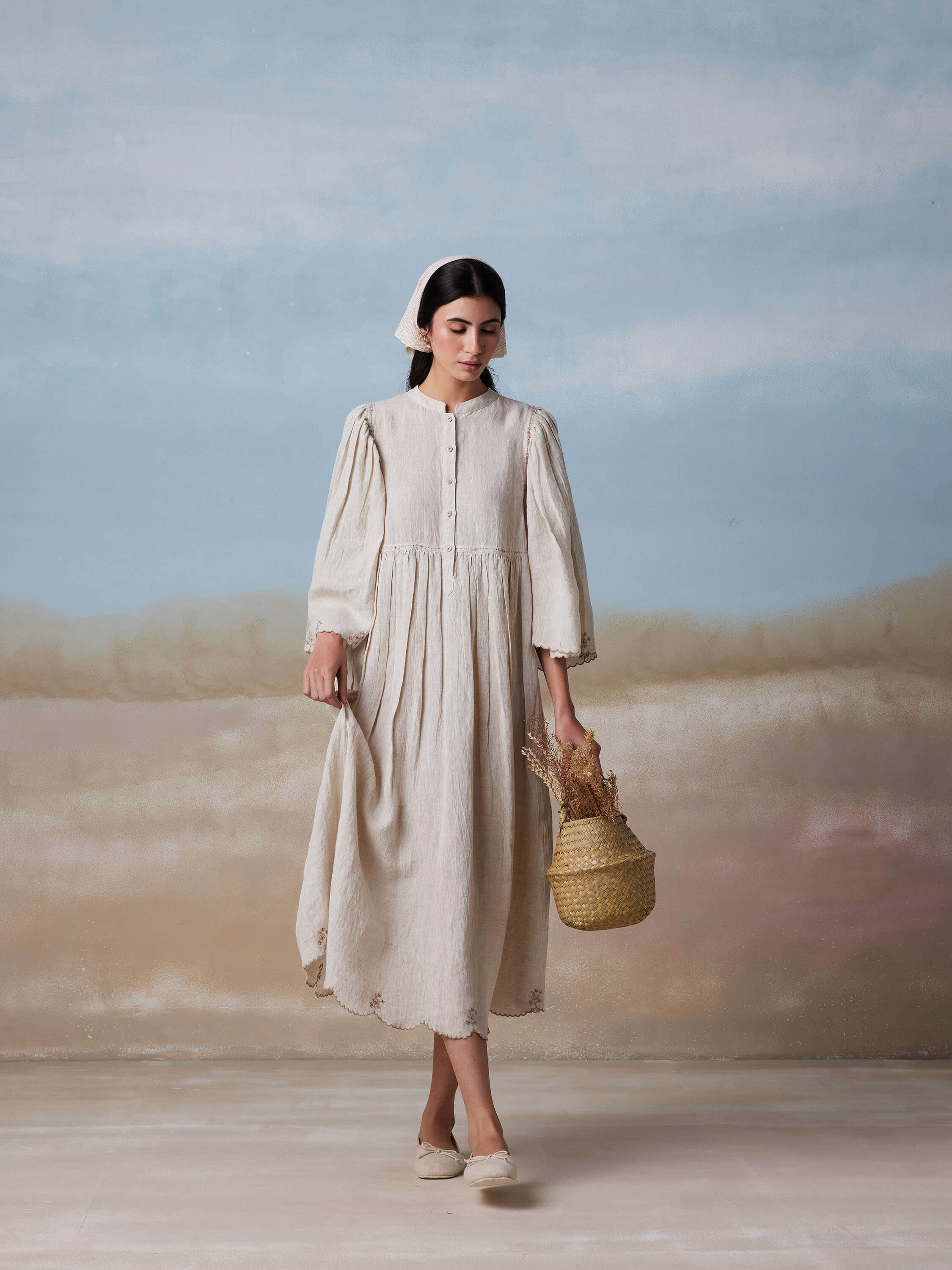 Woman in vintage dress holding wicker basket with dried flowers.