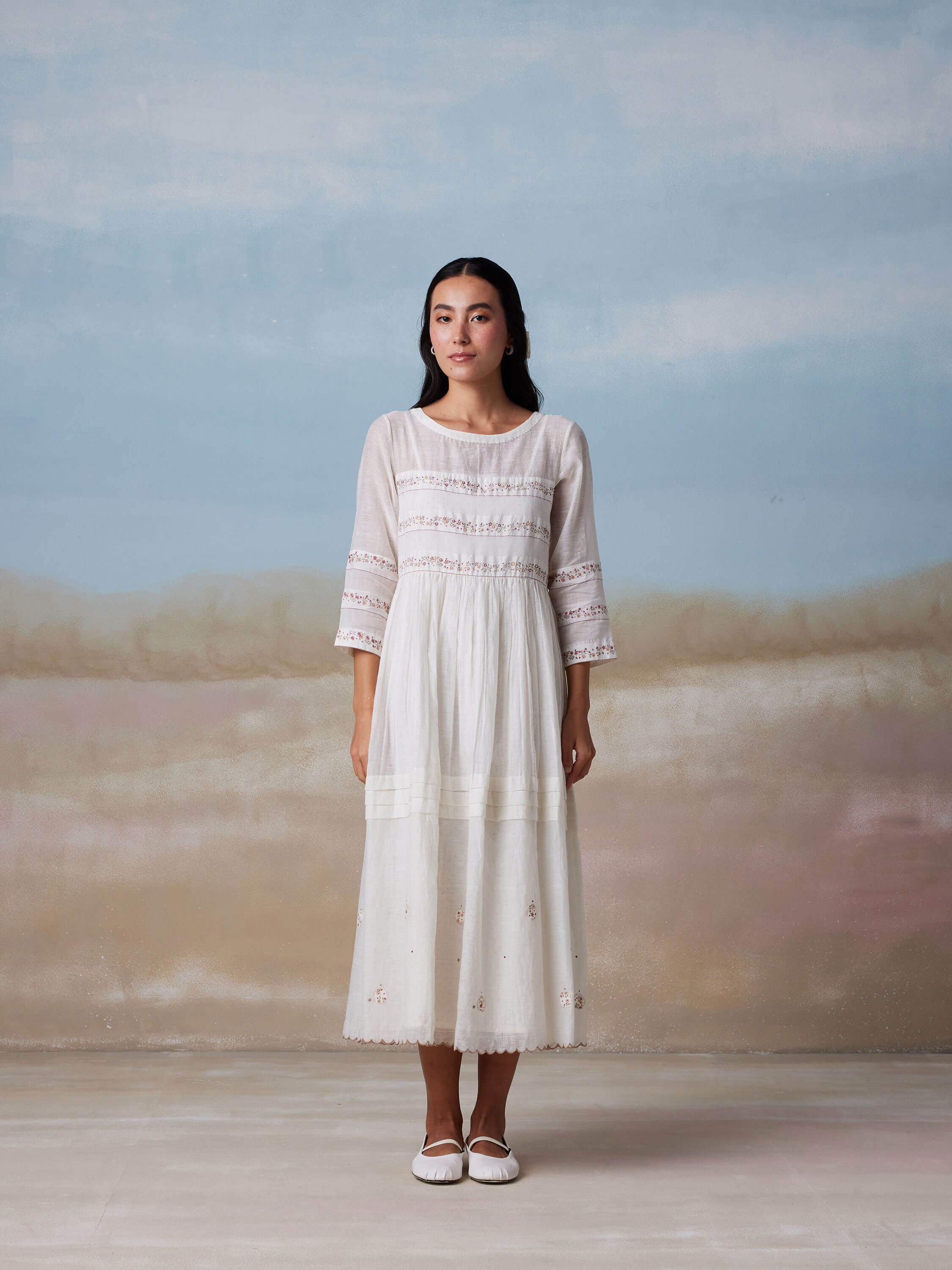 Woman in white long dress standing in minimalist background.