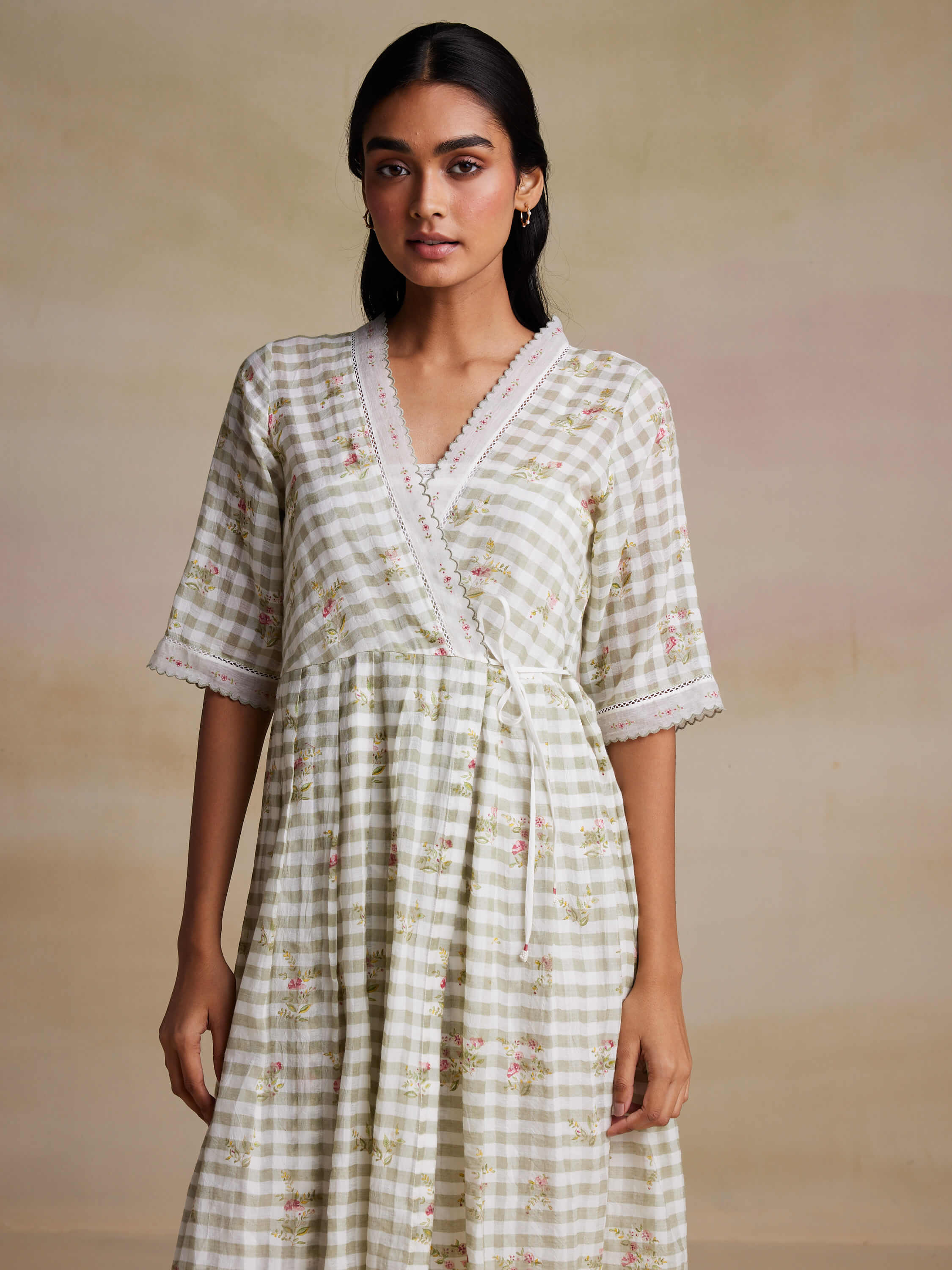 Woman wearing plaid wrap dress with floral pattern, posing against beige background.