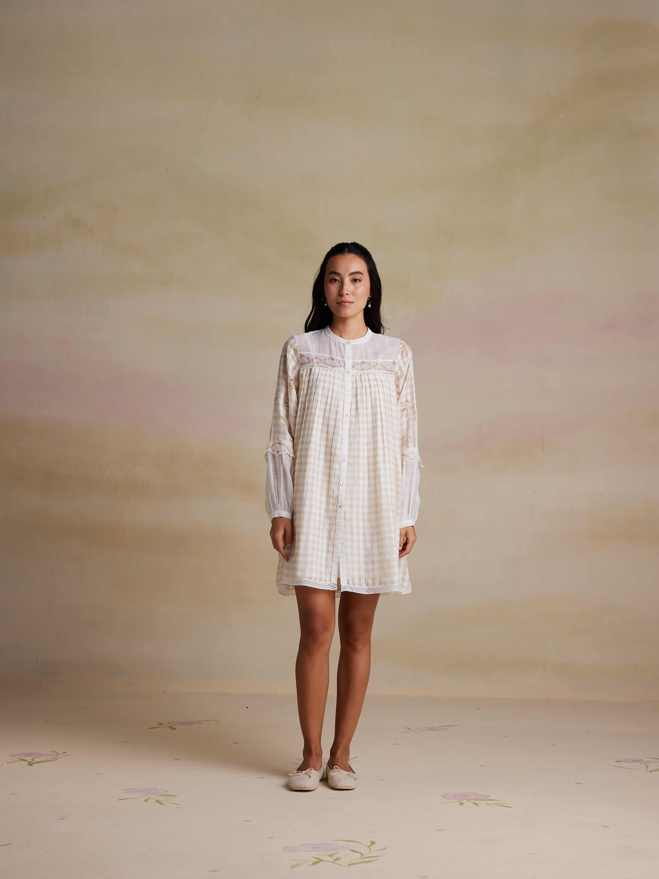 Woman wearing a white checkered dress standing against a pastel background.