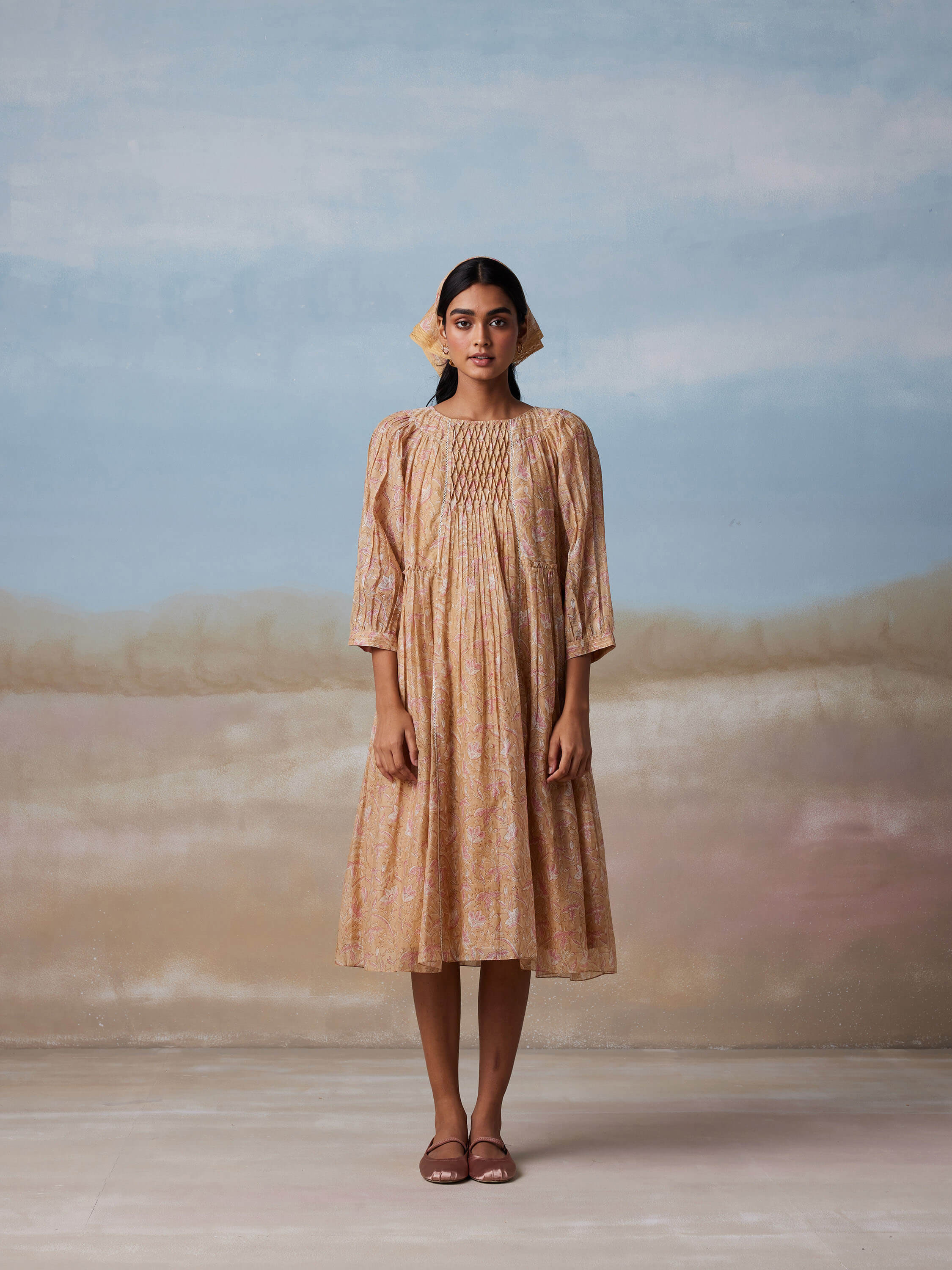 Woman in flowy, floral midi dress poses against a dreamy sky backdrop.