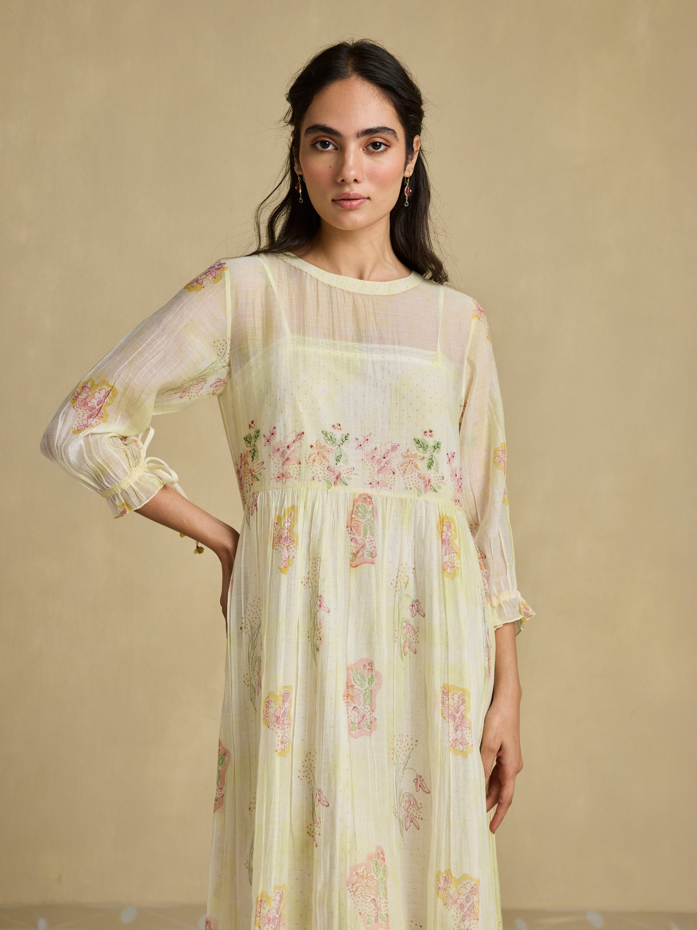 Woman wearing a light yellow floral dress against a beige background