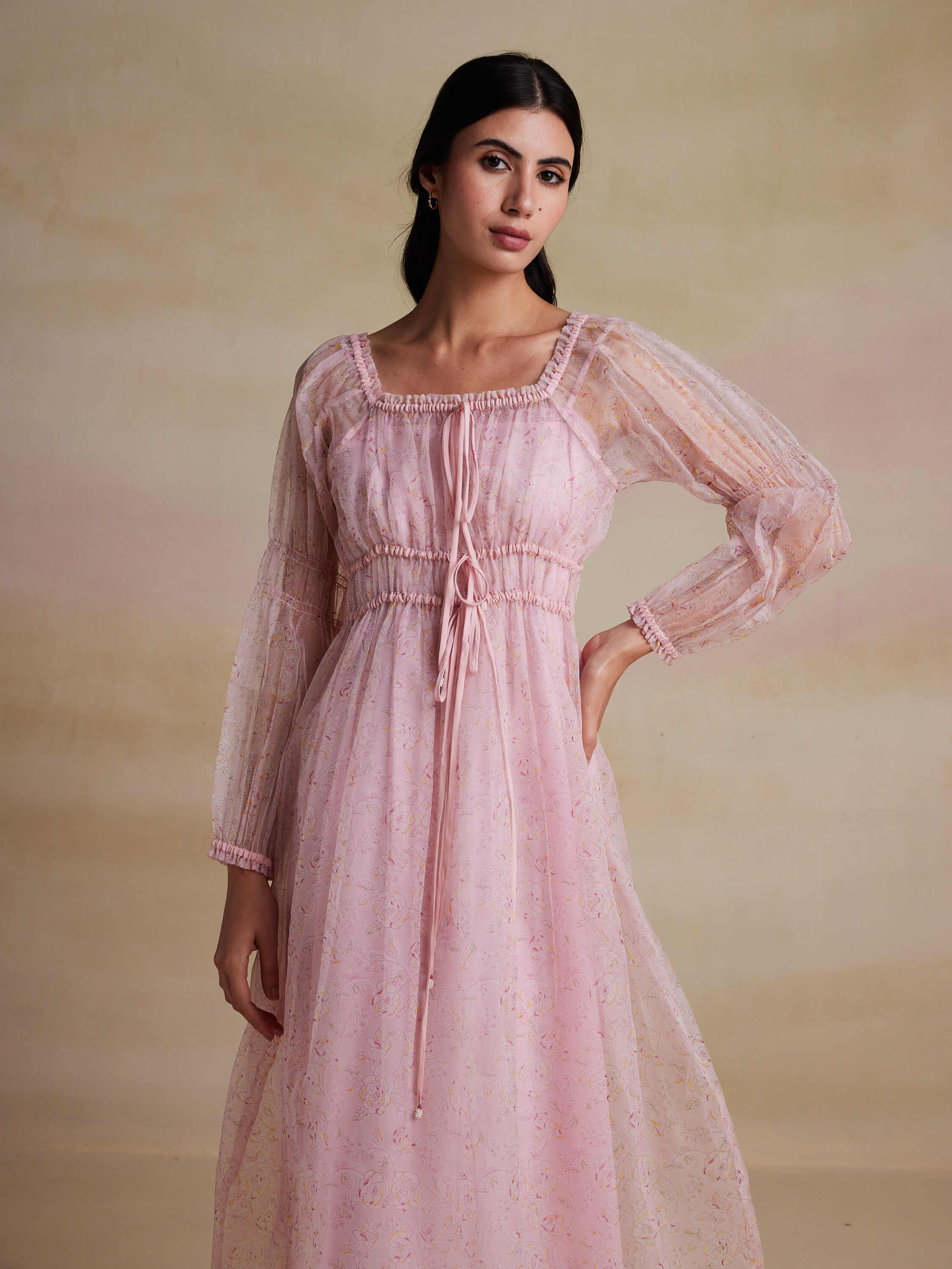 Woman in elegant pink floral dress with sheer sleeves.