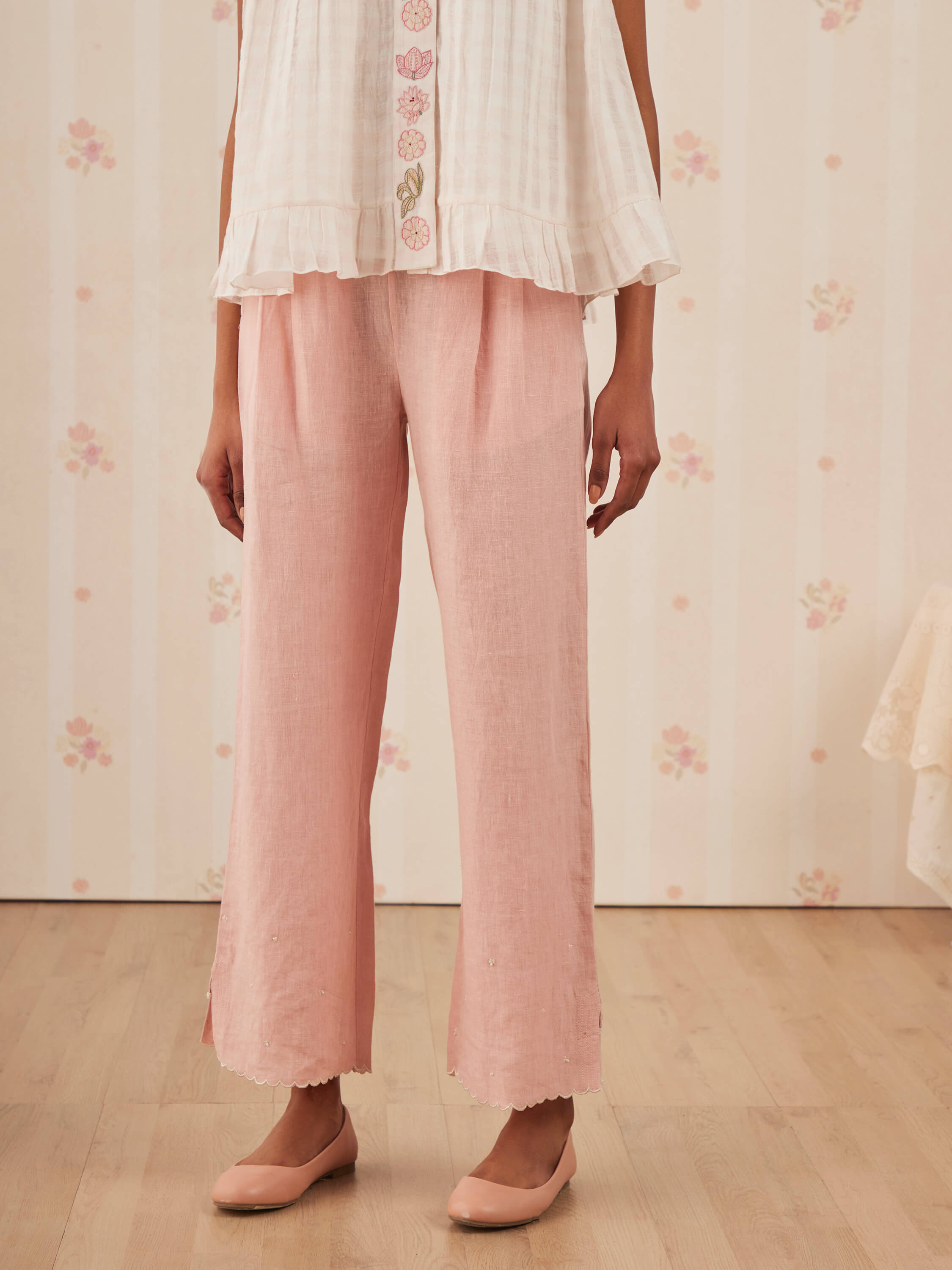 Woman wearing pink pants and white top with floral embroidery.
