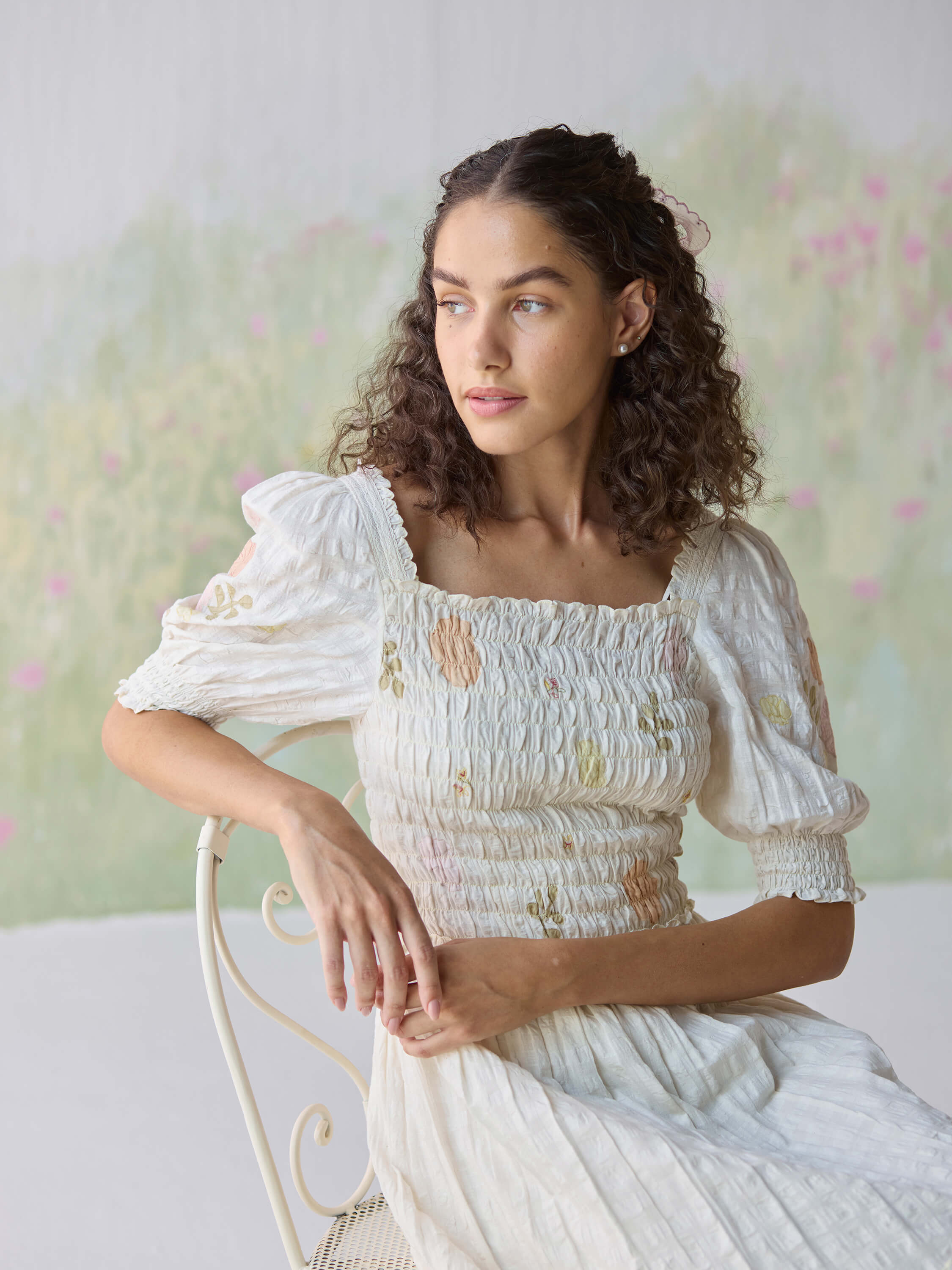 Portrait of woman in white dress sitting on chair, looking away.