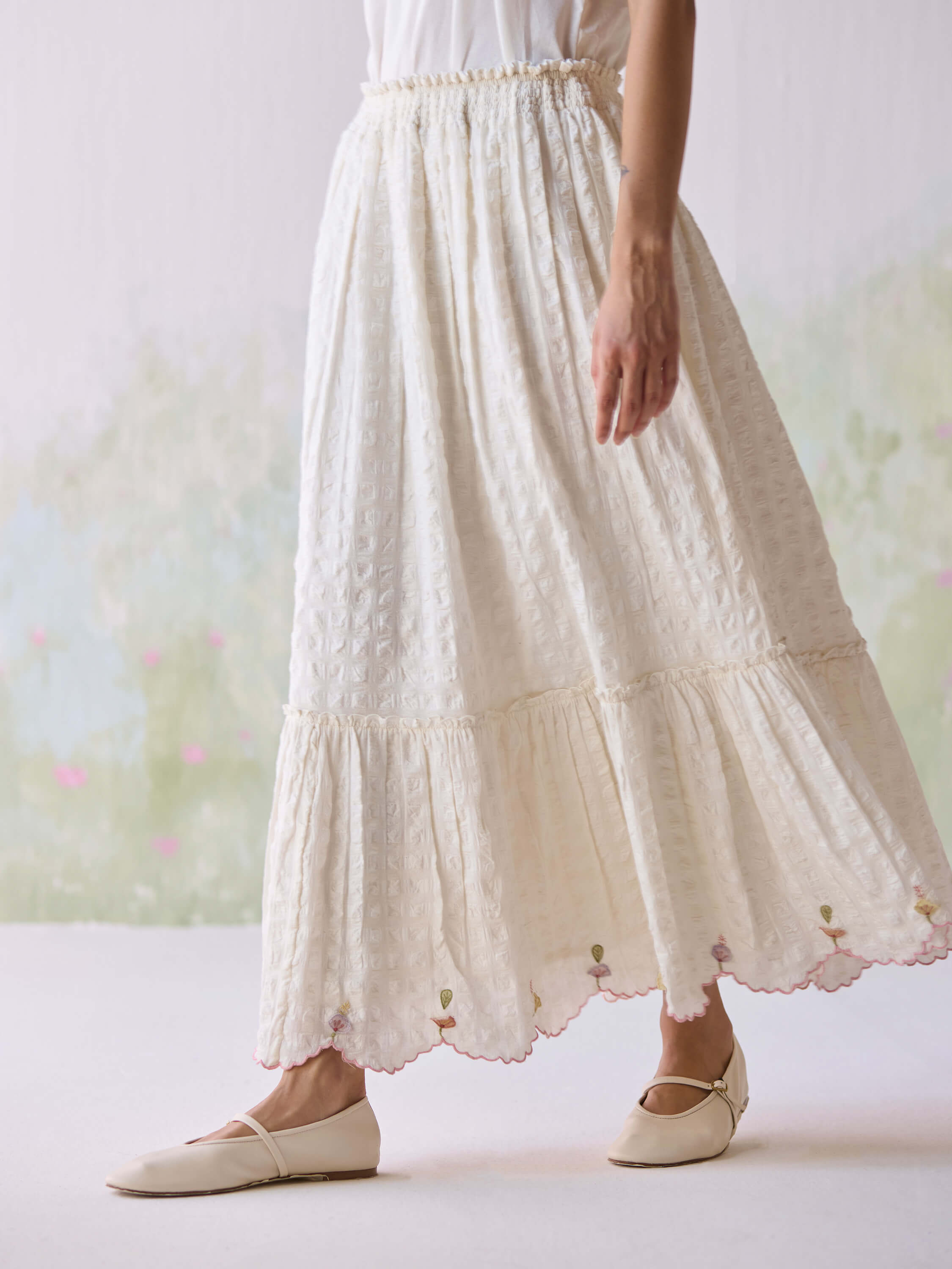 Woman wearing white midi dress with embroidered hemline and beige flats.