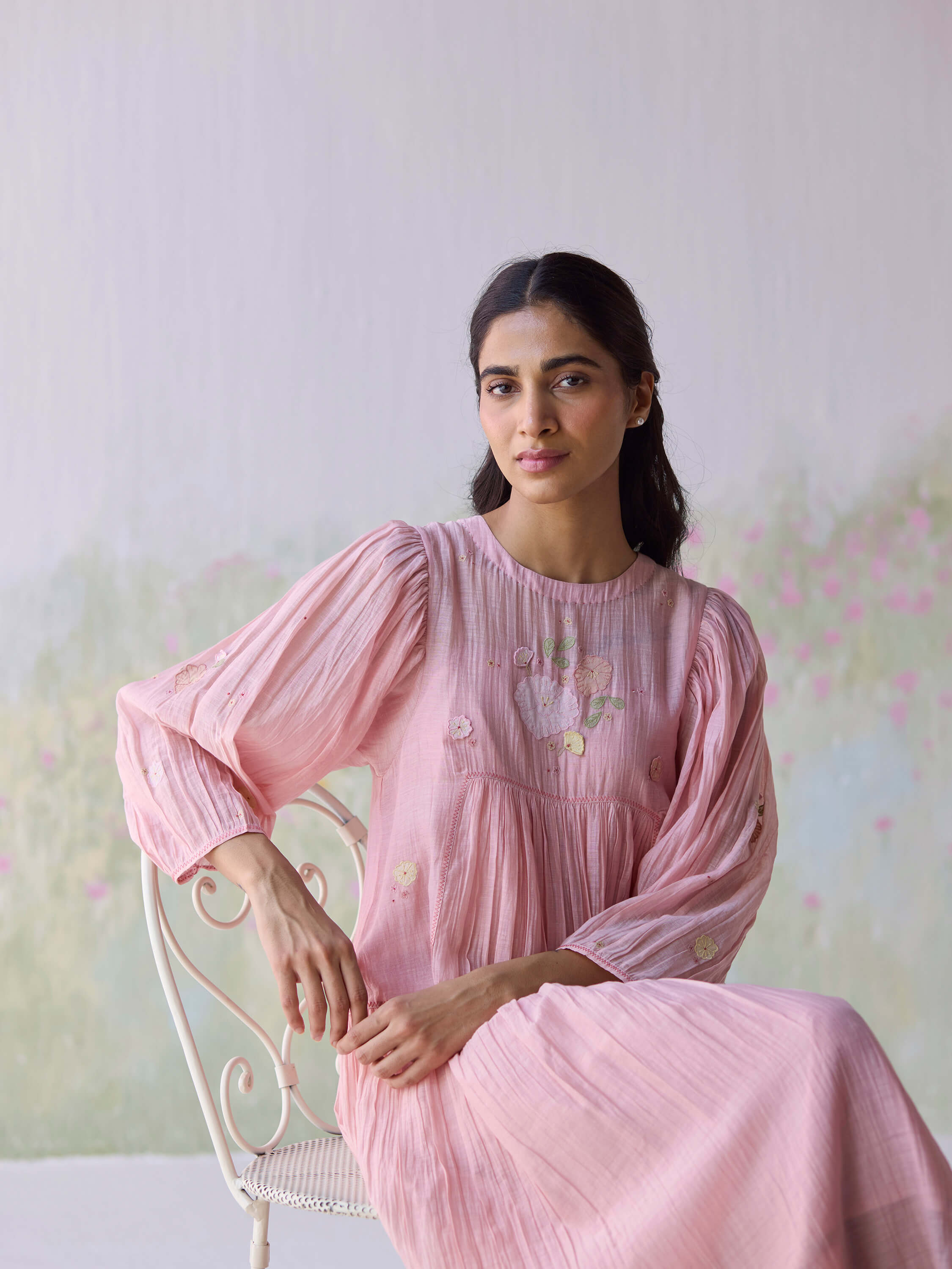 Woman in a pink dress sitting on a white chair.