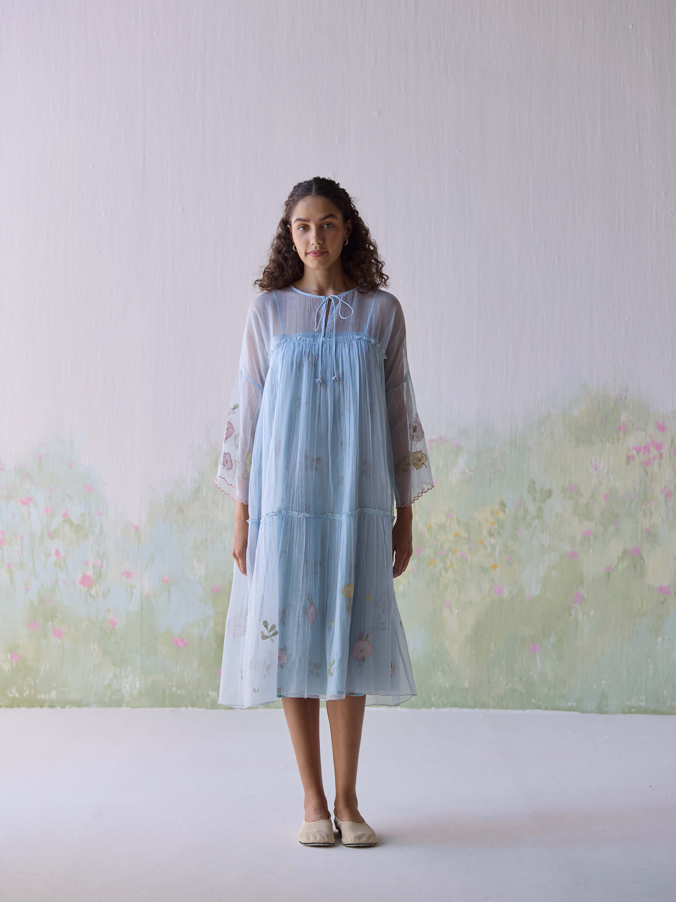 Young woman in a light blue floral dress standing indoors.