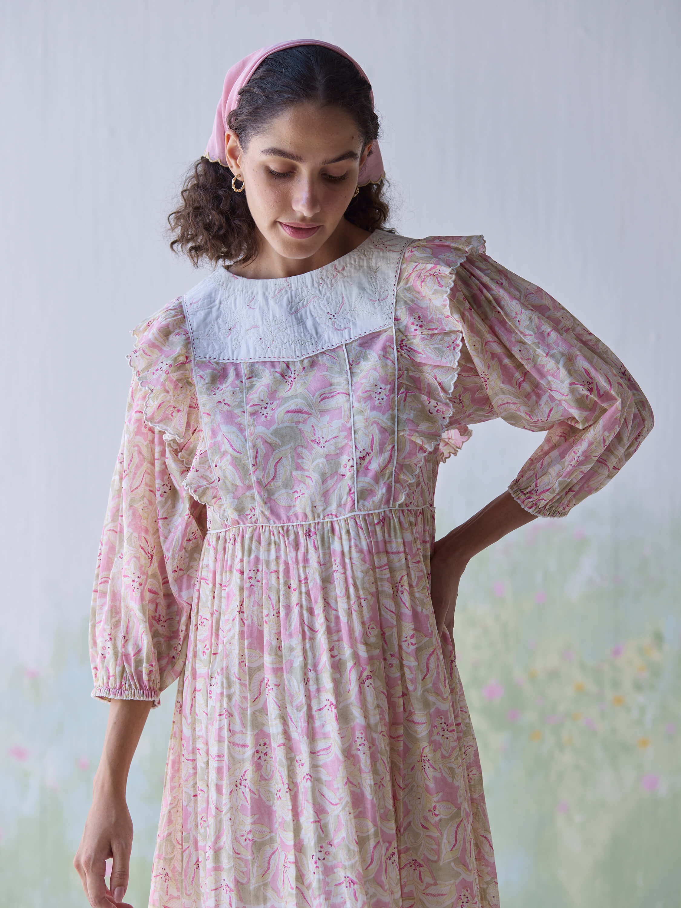 Woman in floral vintage dress with pink headscarf and neutral background.