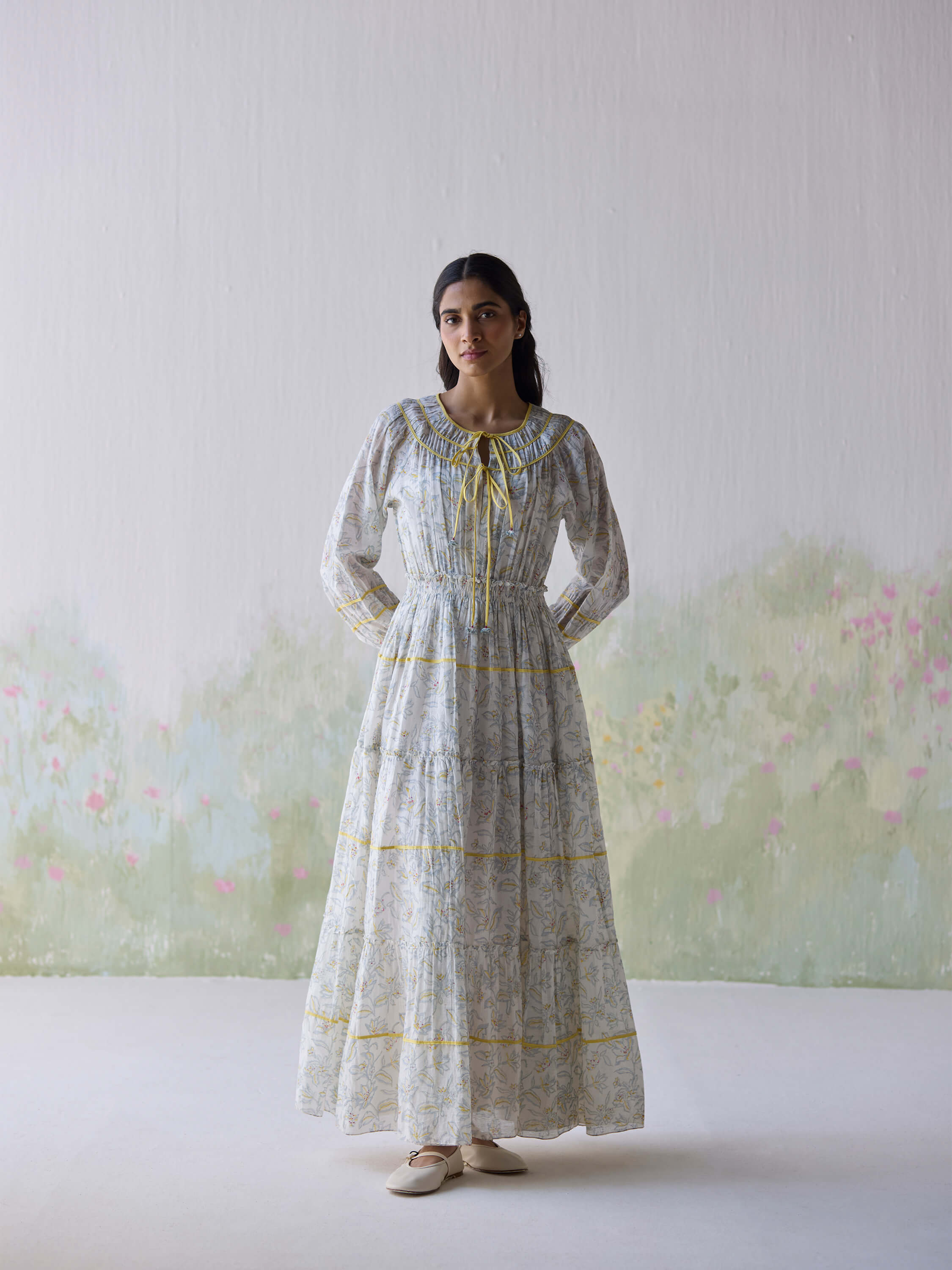 Woman in floral long dress standing against a floral background.