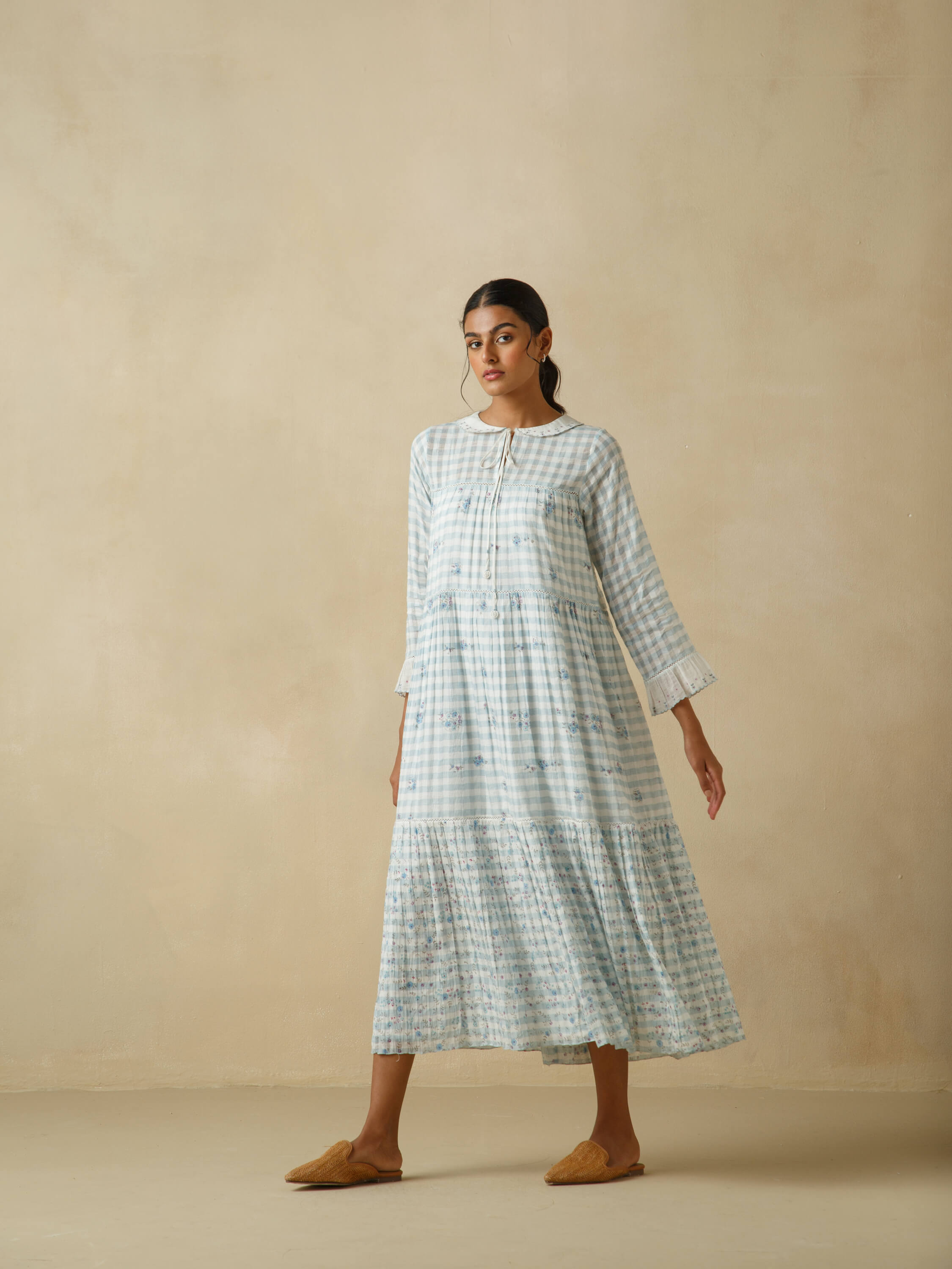 Woman in a long, flowy blue plaid dress with a beige background.