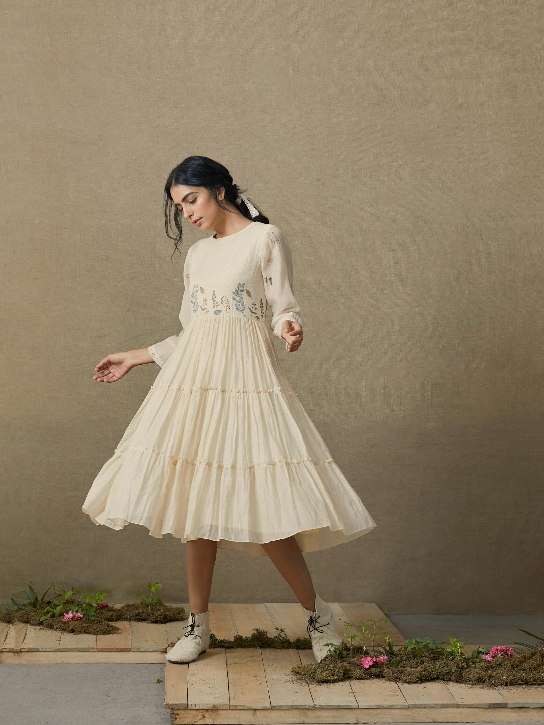 Woman in flowy beige dress twirling on wooden platform with floral accents.