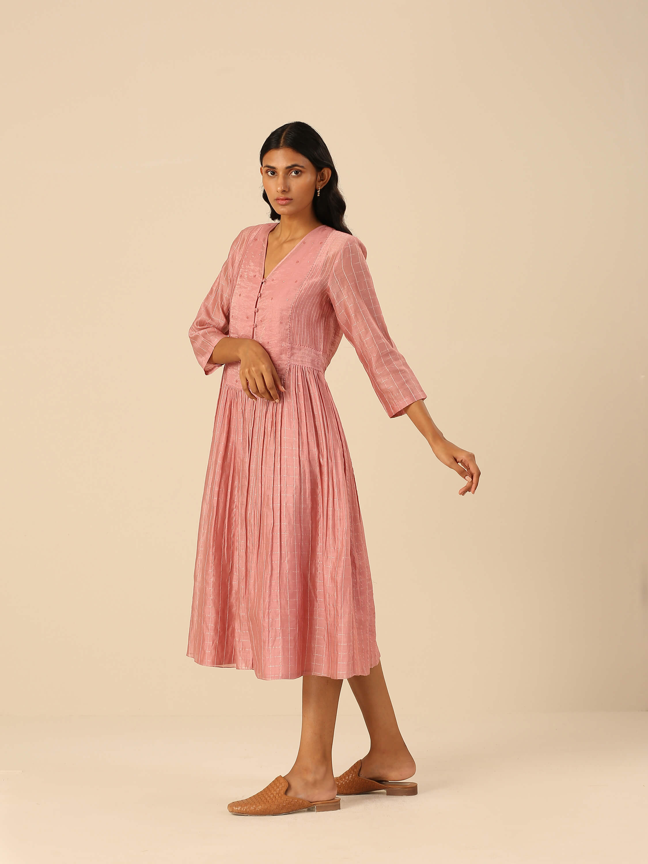 Model wearing a pink, long-sleeved, midi dress with buttons and pleats.