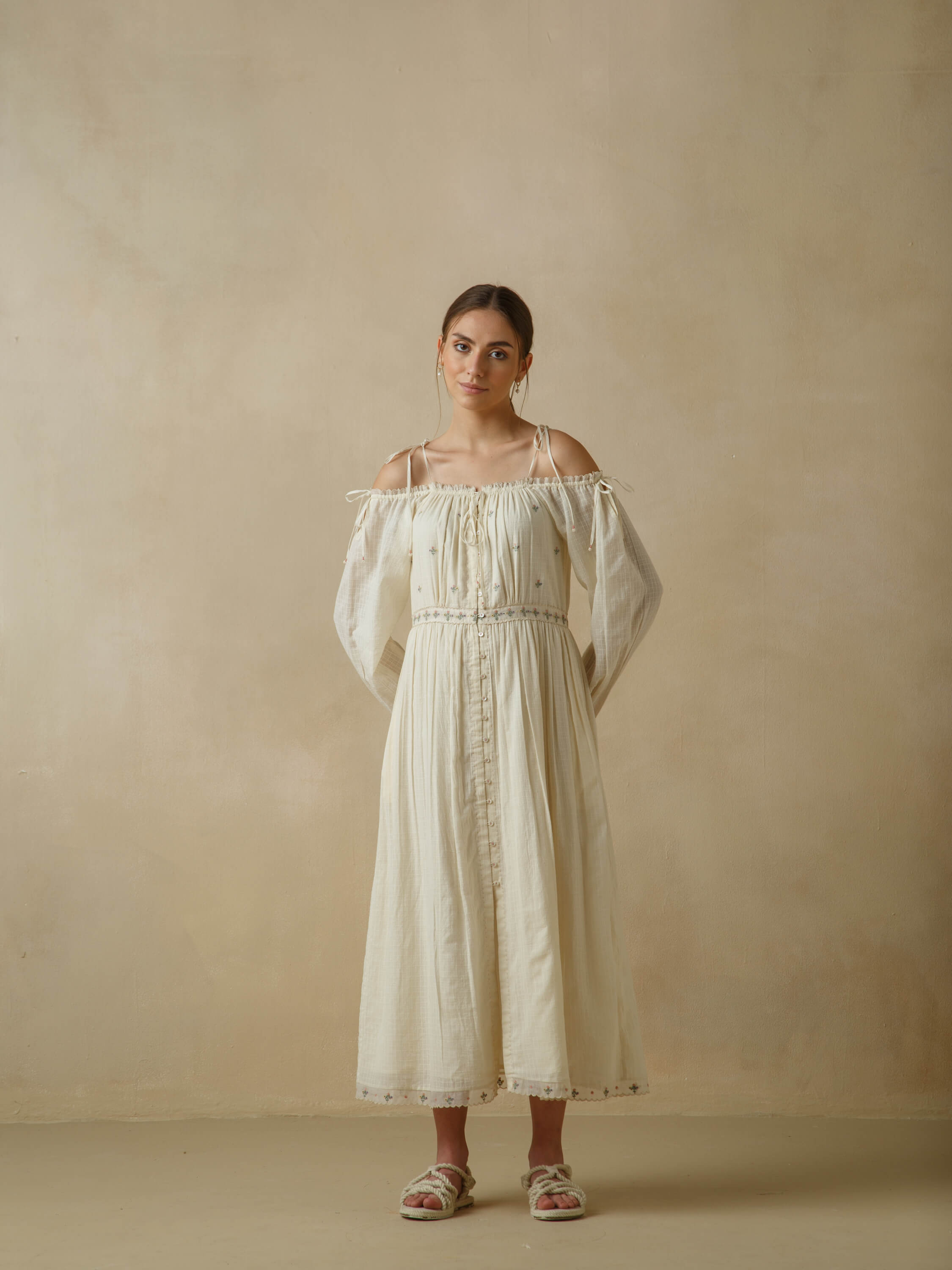 Woman wearing off-shoulder cream dress, minimalist beige background.