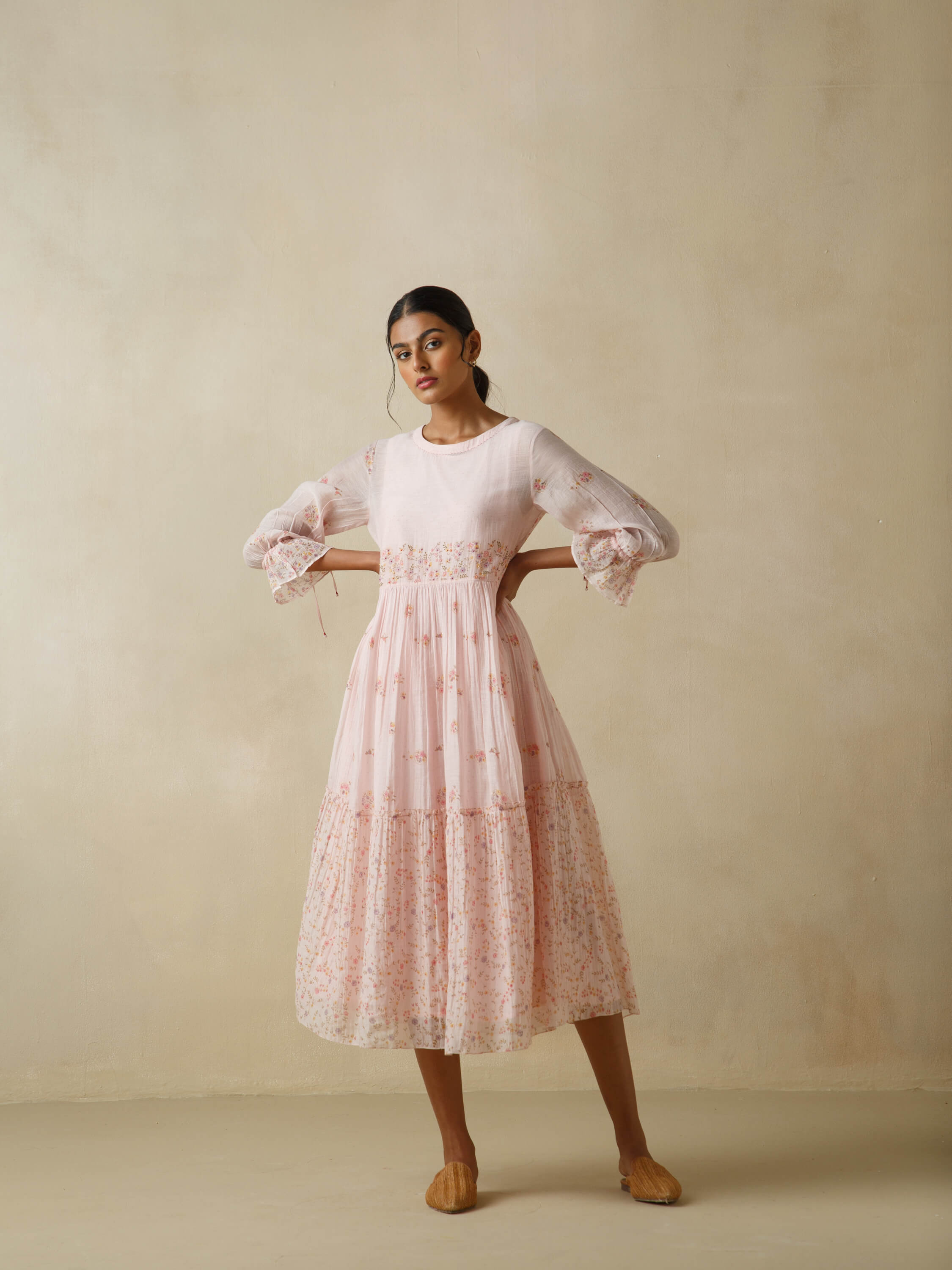 Woman in elegant long-sleeved pink floral dress standing against beige background.