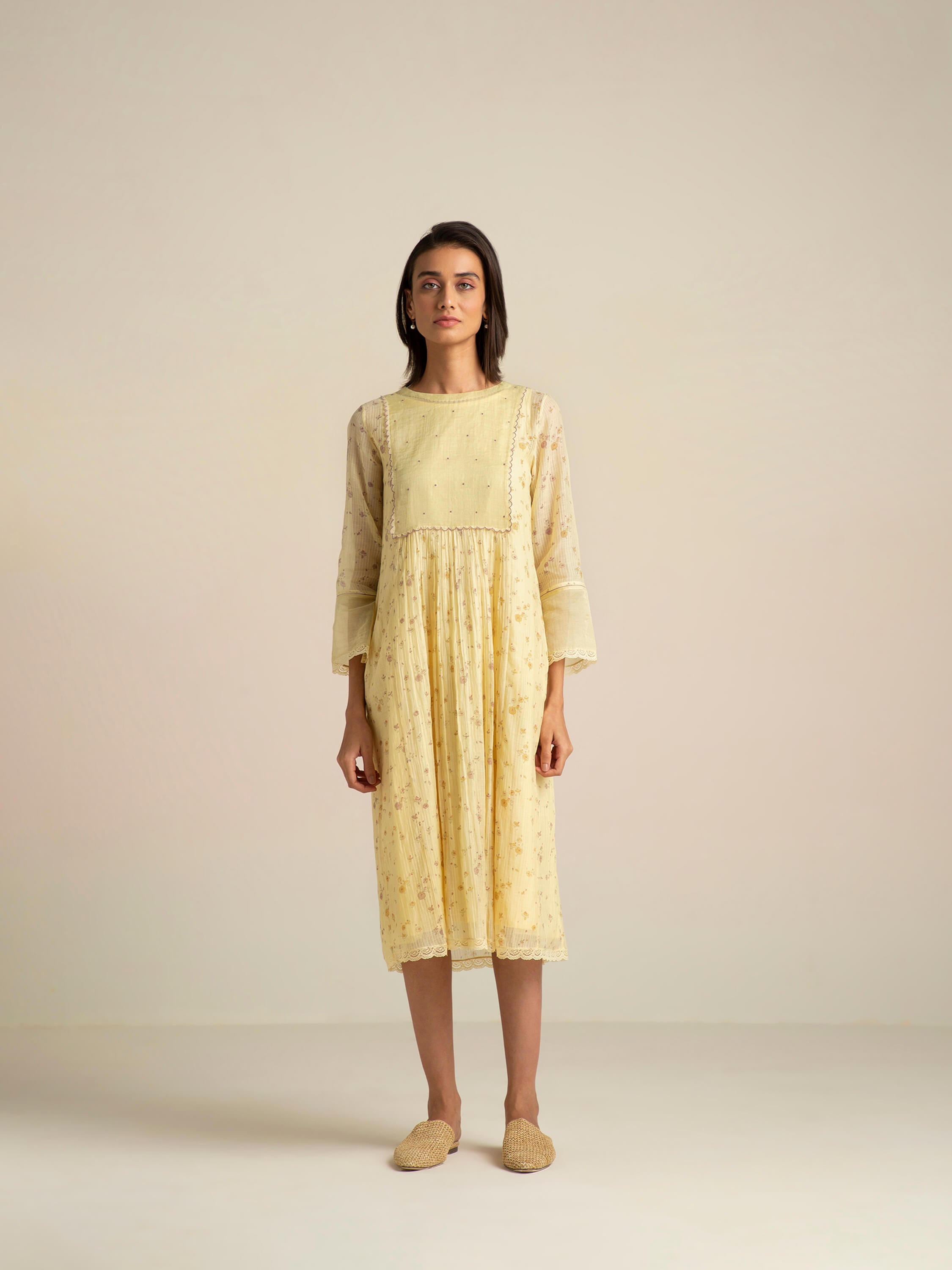 Woman wearing a yellow dress with sheer sleeves in a minimalistic setting.
