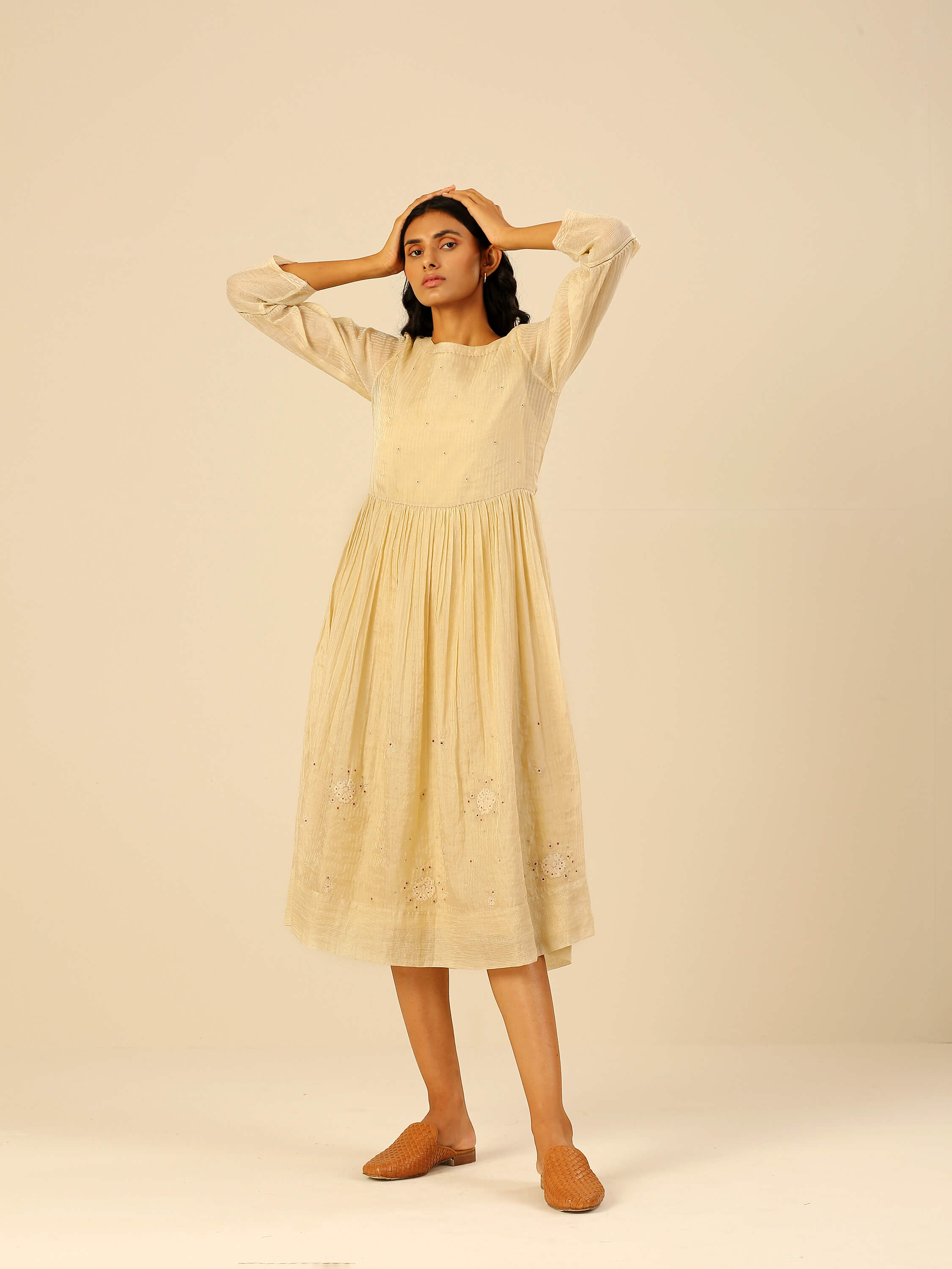 Woman modeling beige long sleeve dress with intricate detailing.