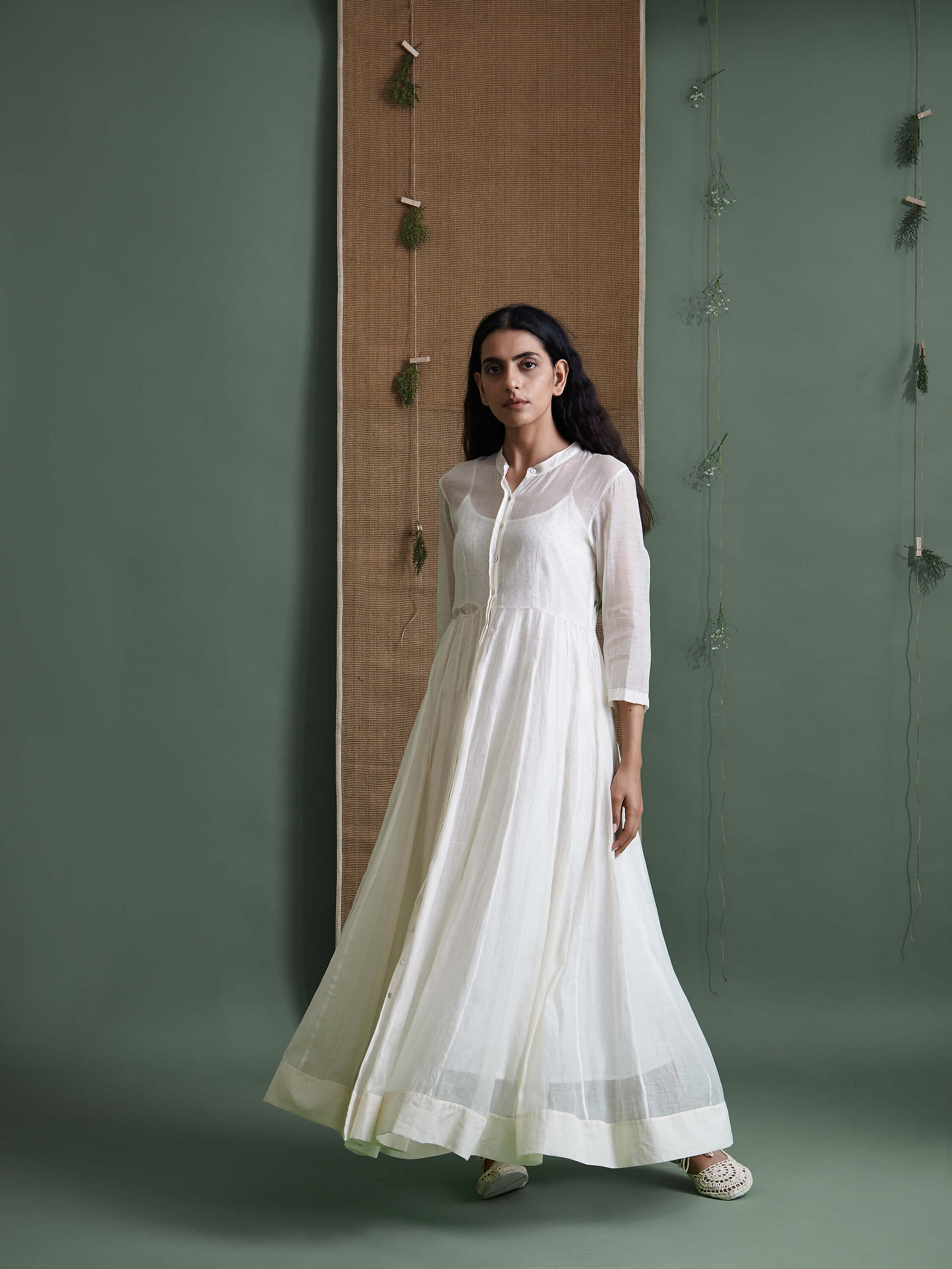 Woman wearing long white dress in minimalist green background.