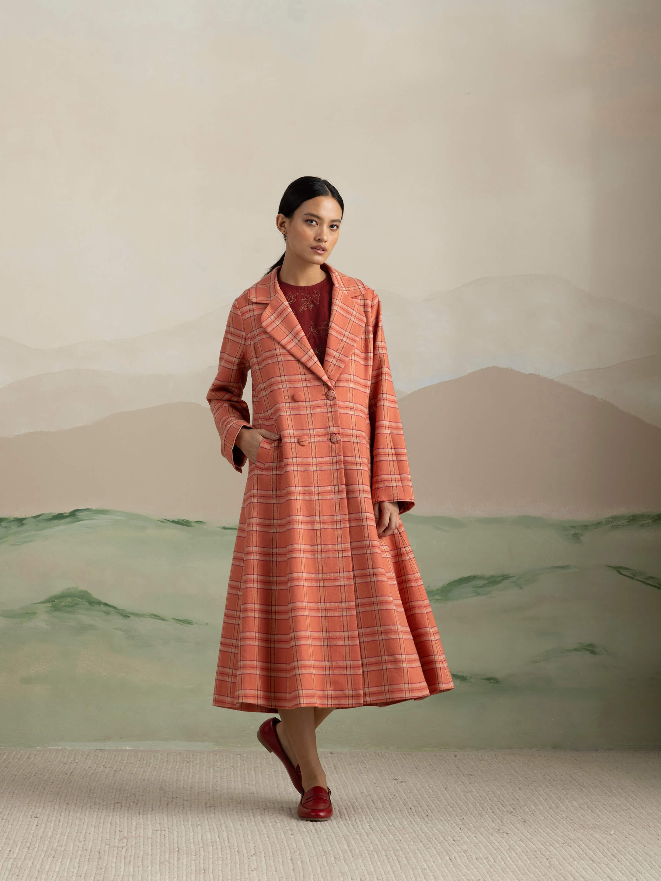 Woman wearing a stylish plaid coat in front of scenic mural.