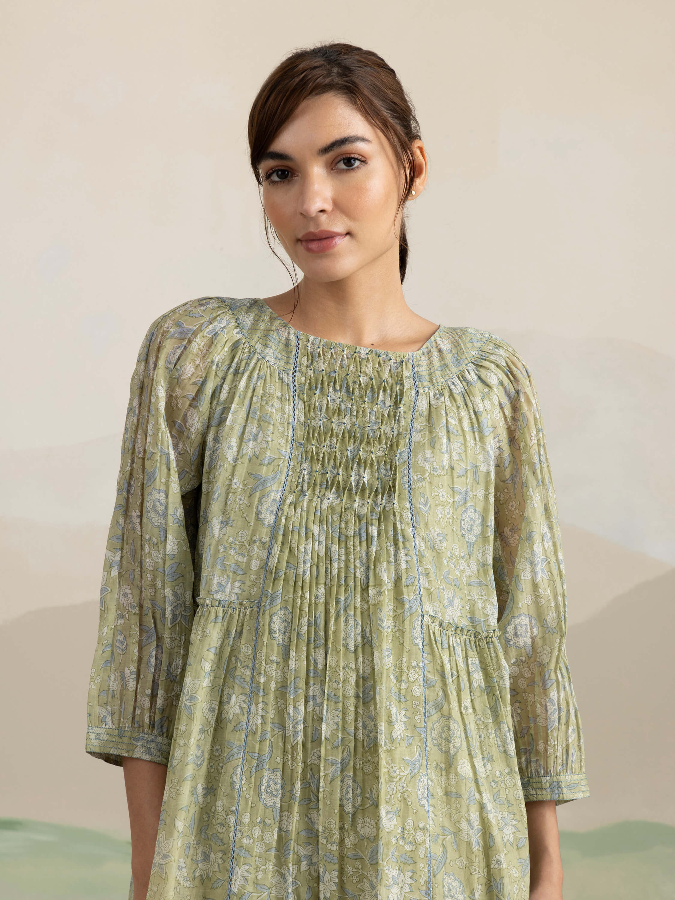 Woman wearing a light green floral dress with smocked detailing.