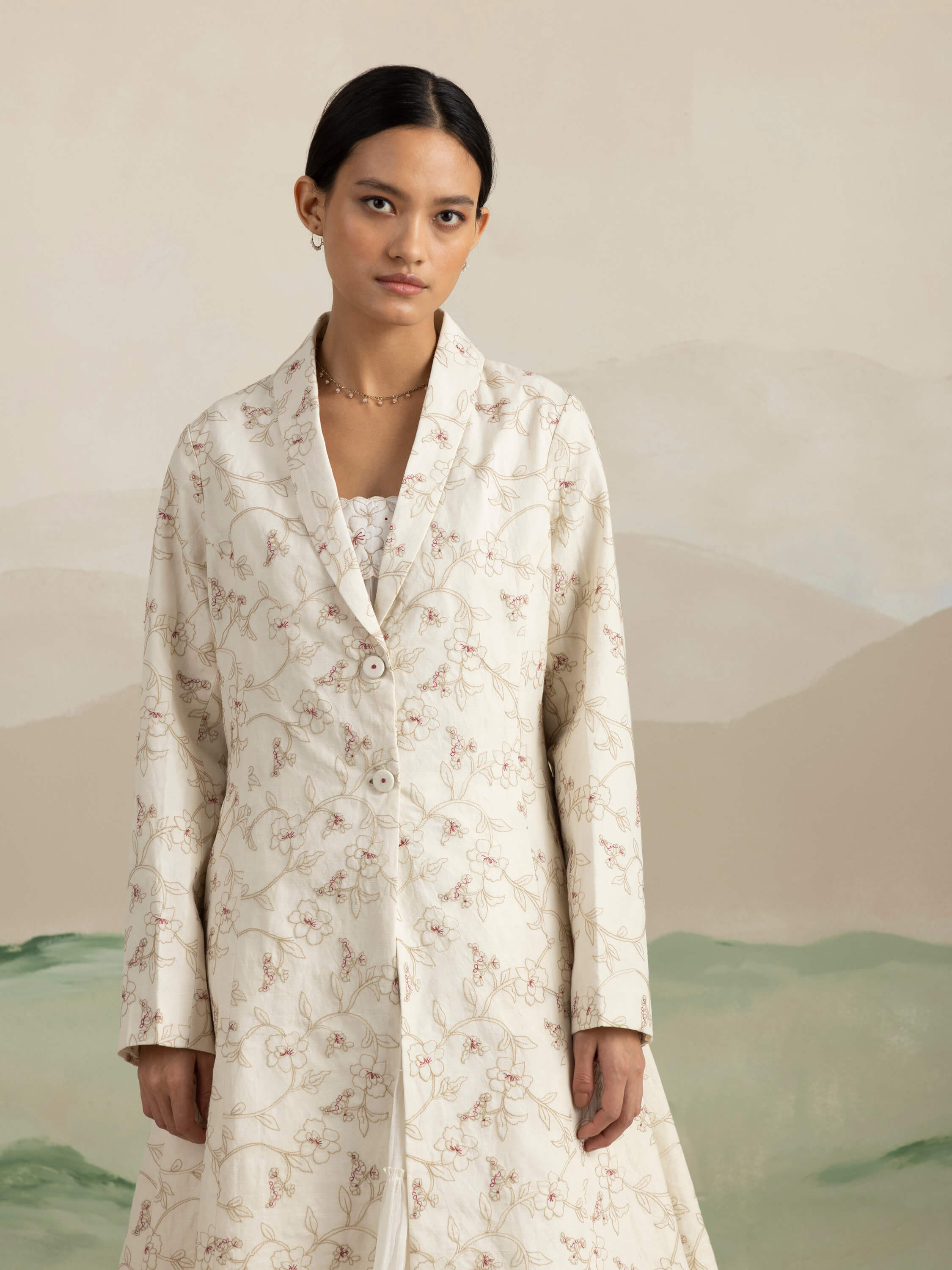 Woman wearing an elegant floral-embroidered coat, neutral background.
