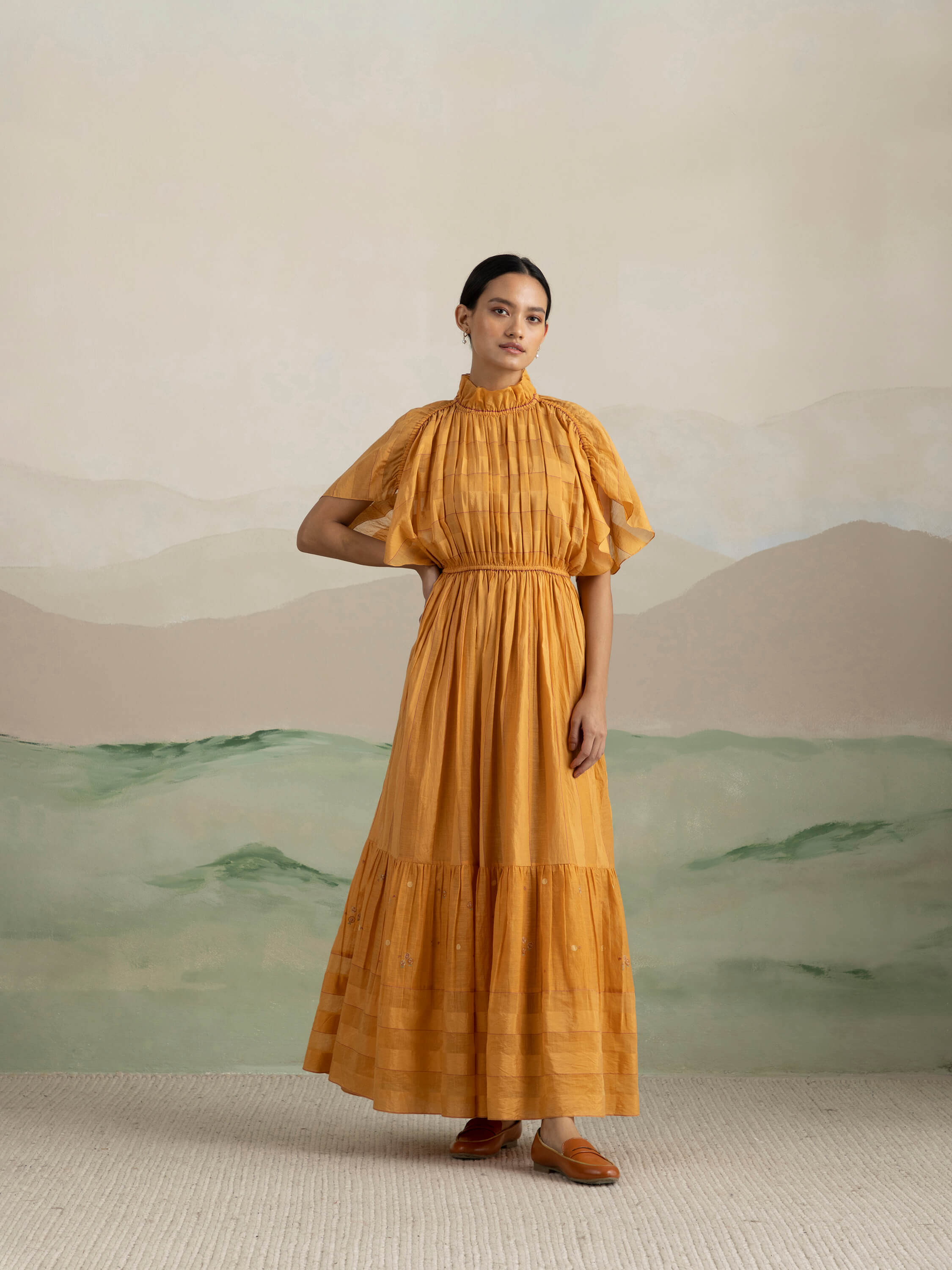 Woman in a flowing mustard yellow dress with serene backdrop.