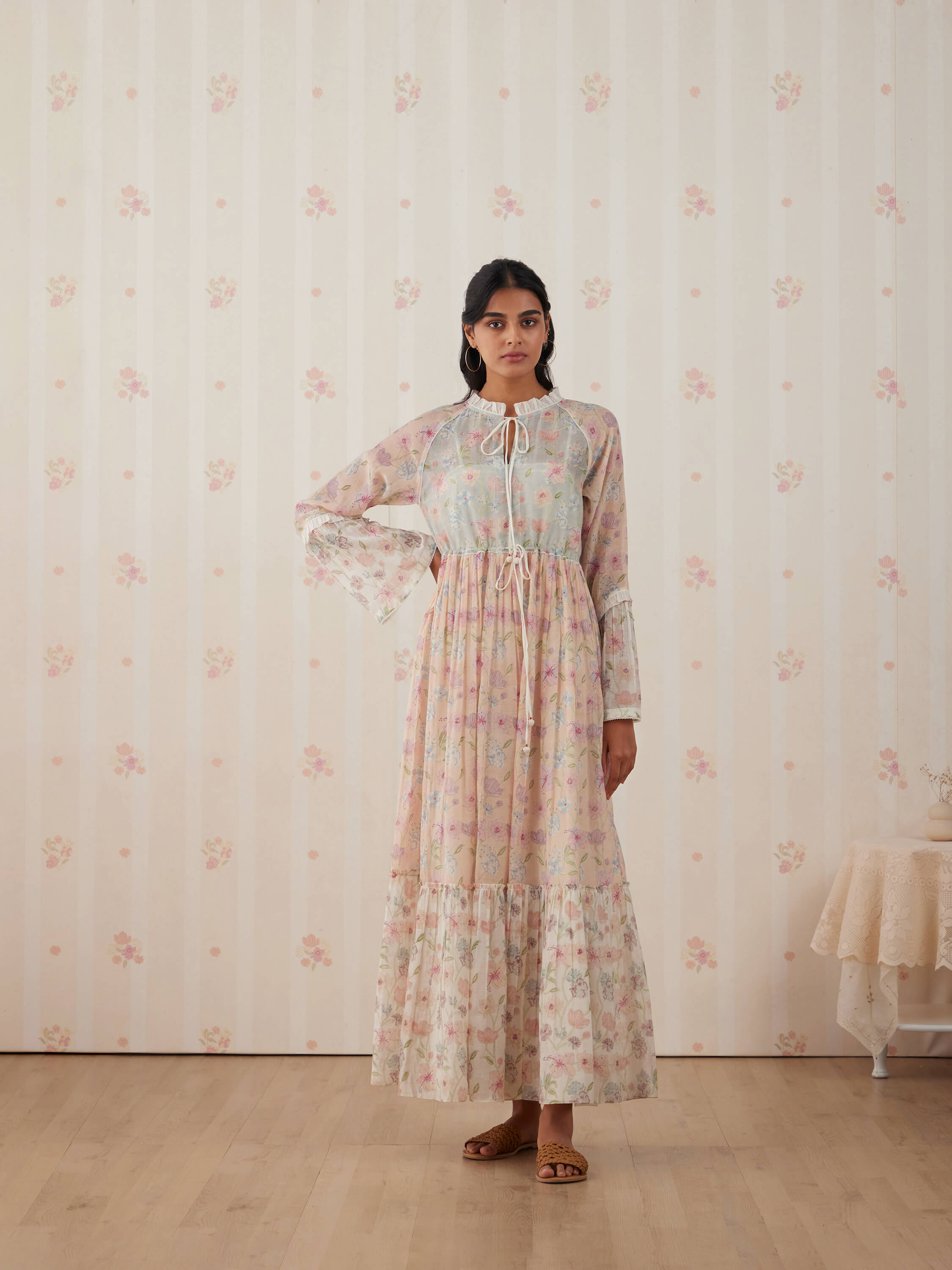 Woman in floral maxi dress posing against vintage wallpaper background.