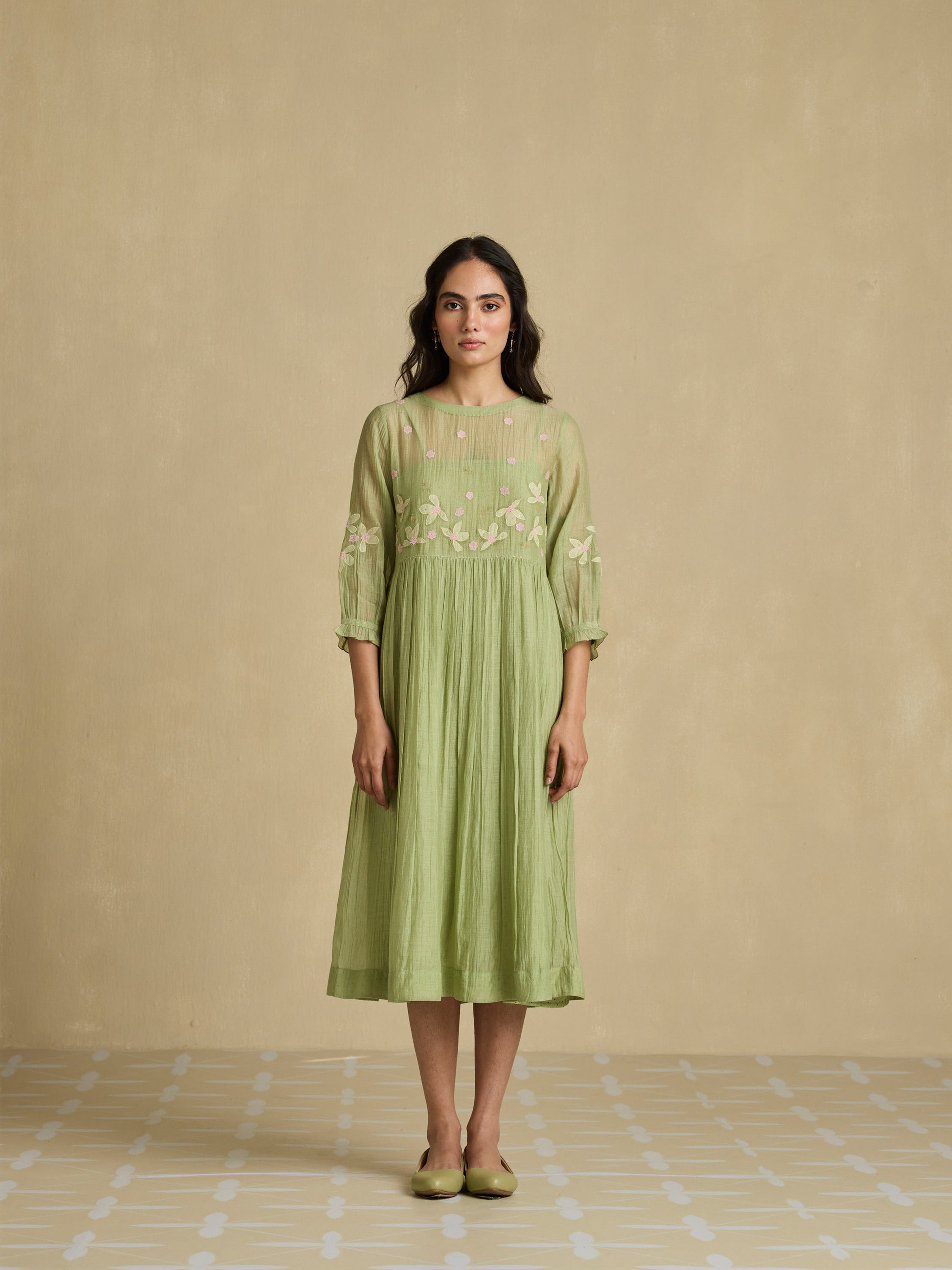 Woman wearing a green dress with floral embroidery on a beige background