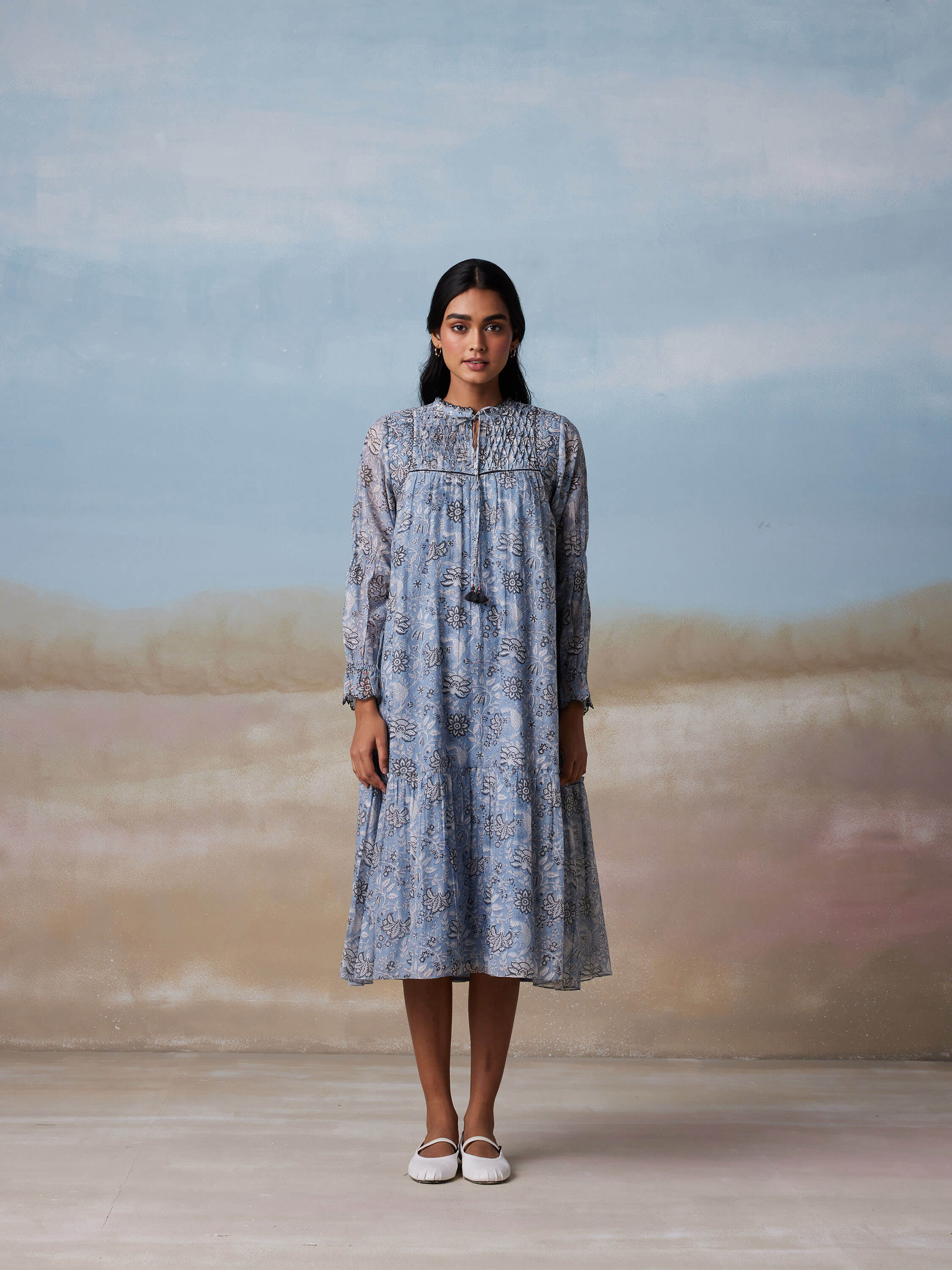 Woman in blue floral dress standing against a soft pastel background.