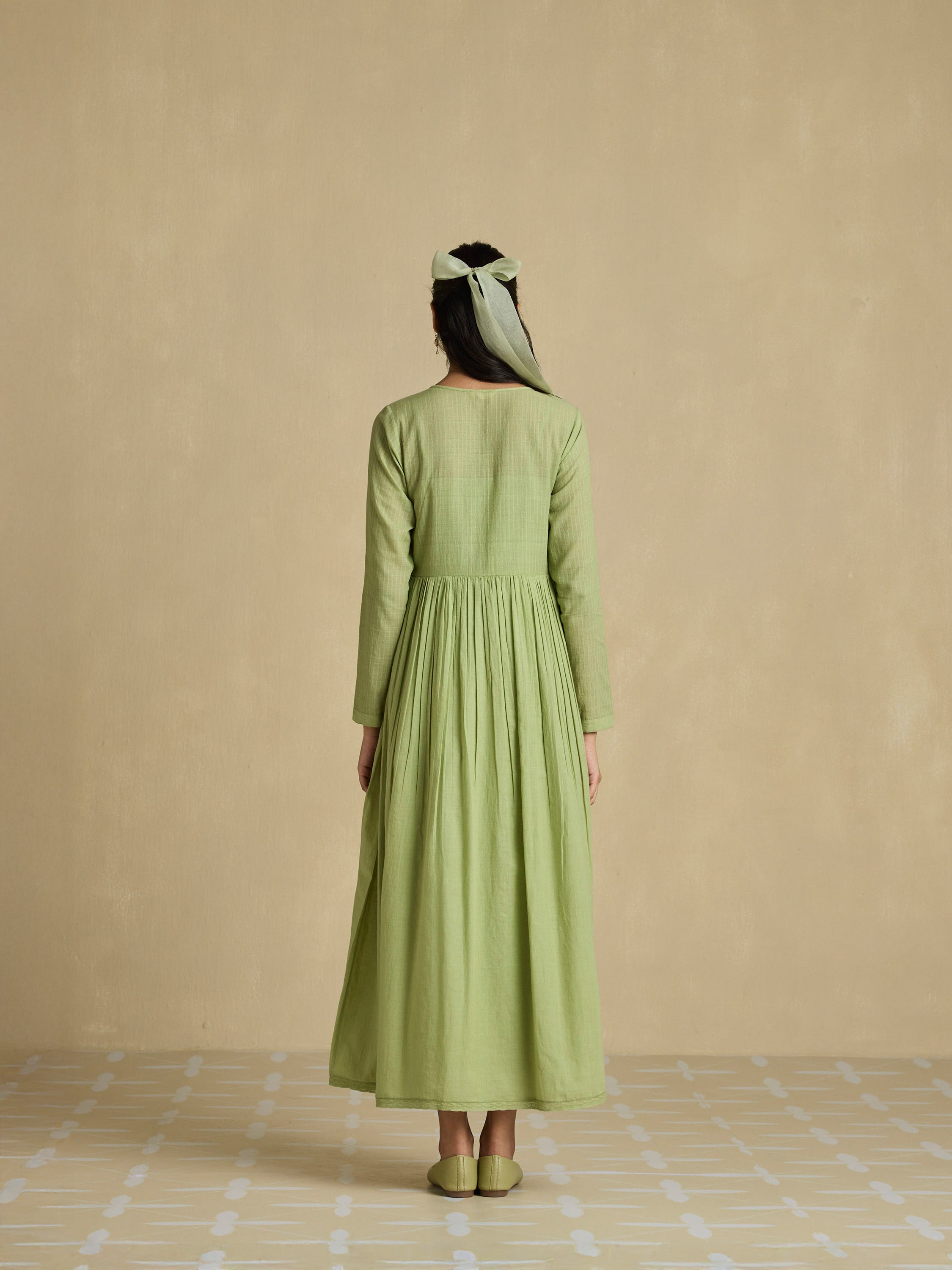 Woman wearing a green dress standing against a beige wall.