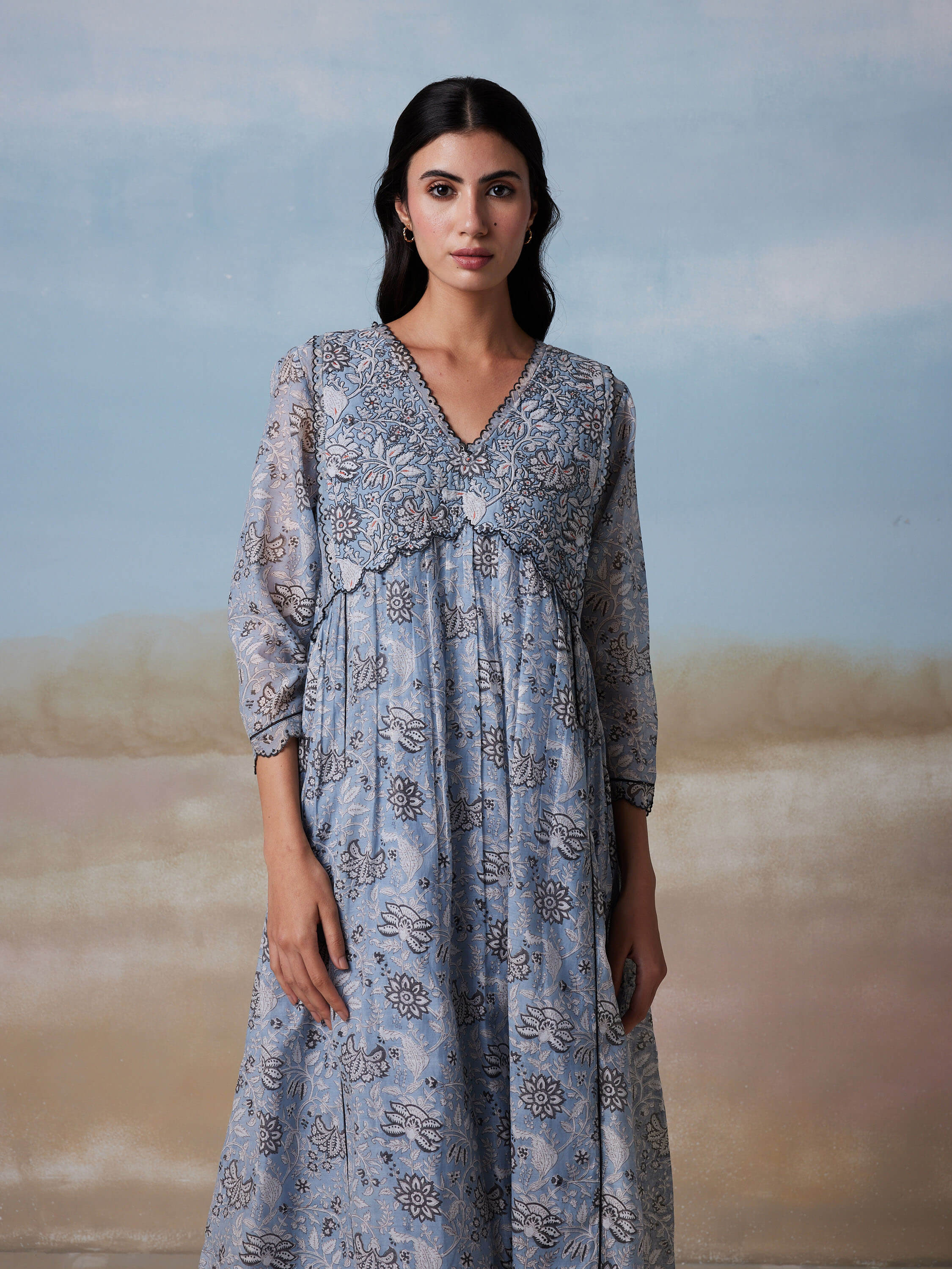 Woman wearing a blue floral dress with intricate patterns.