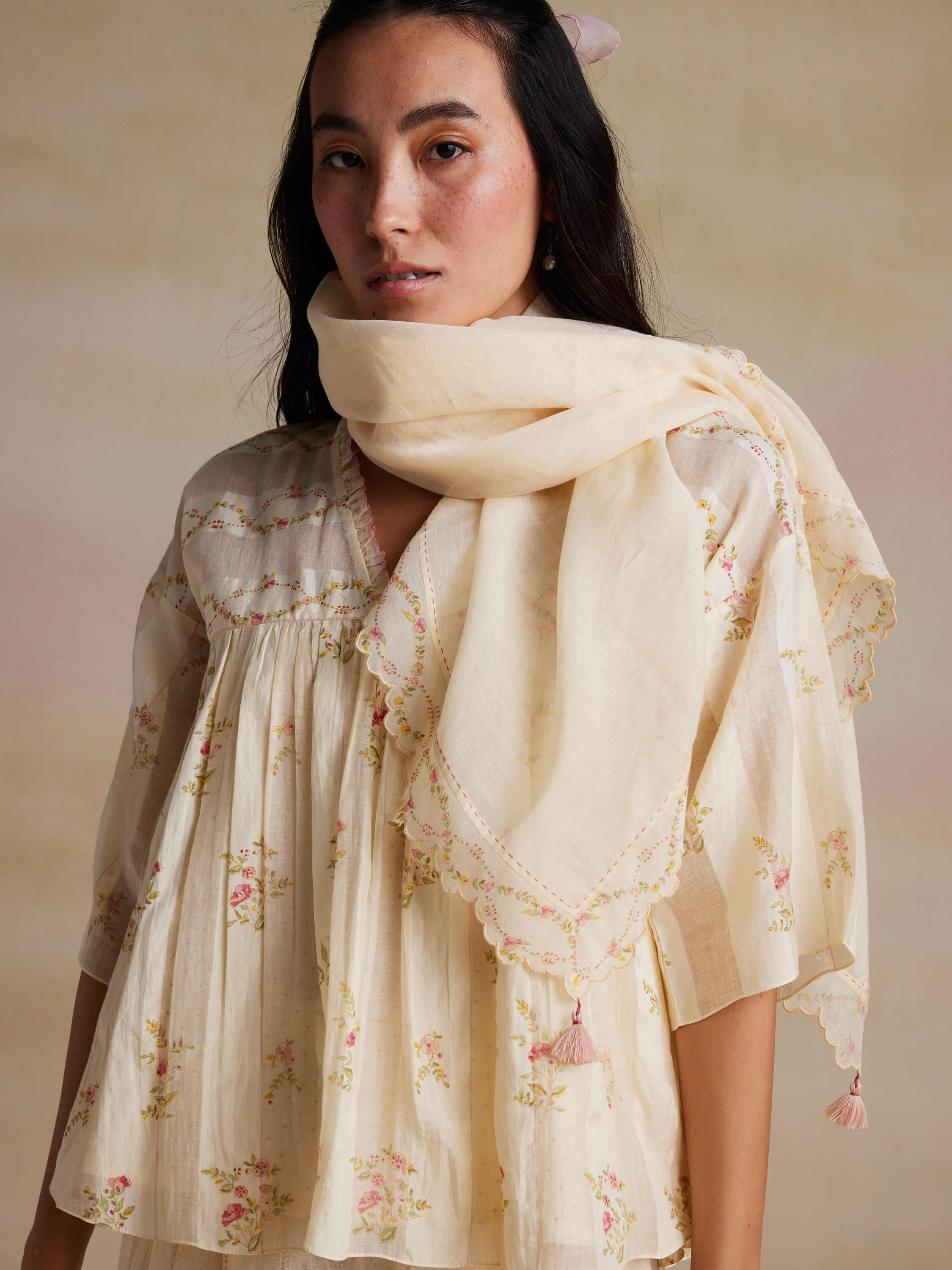 Woman in floral embroidered top and scarf, beige background.