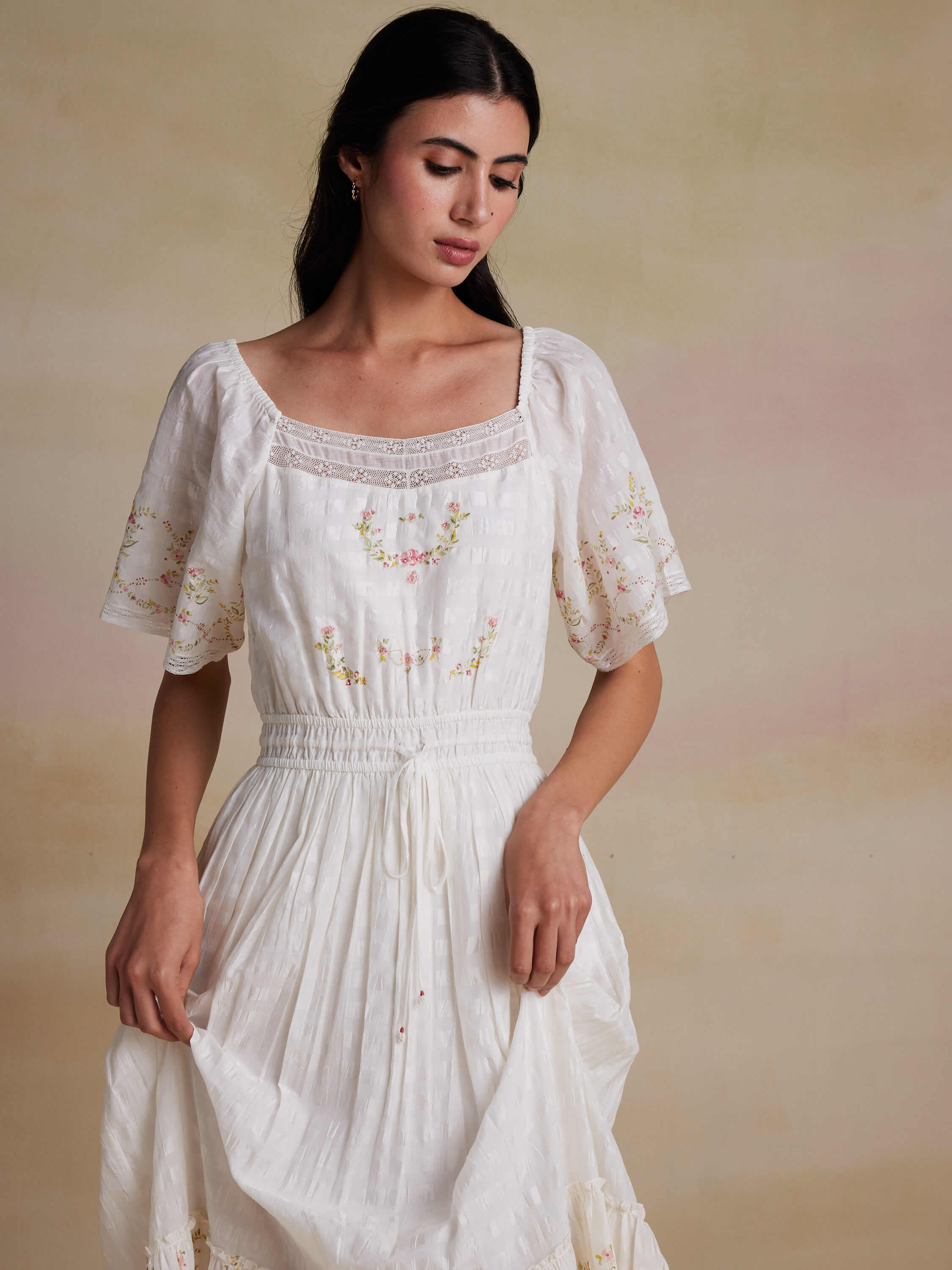 Woman wearing a white embroidered dress with lace detailing.