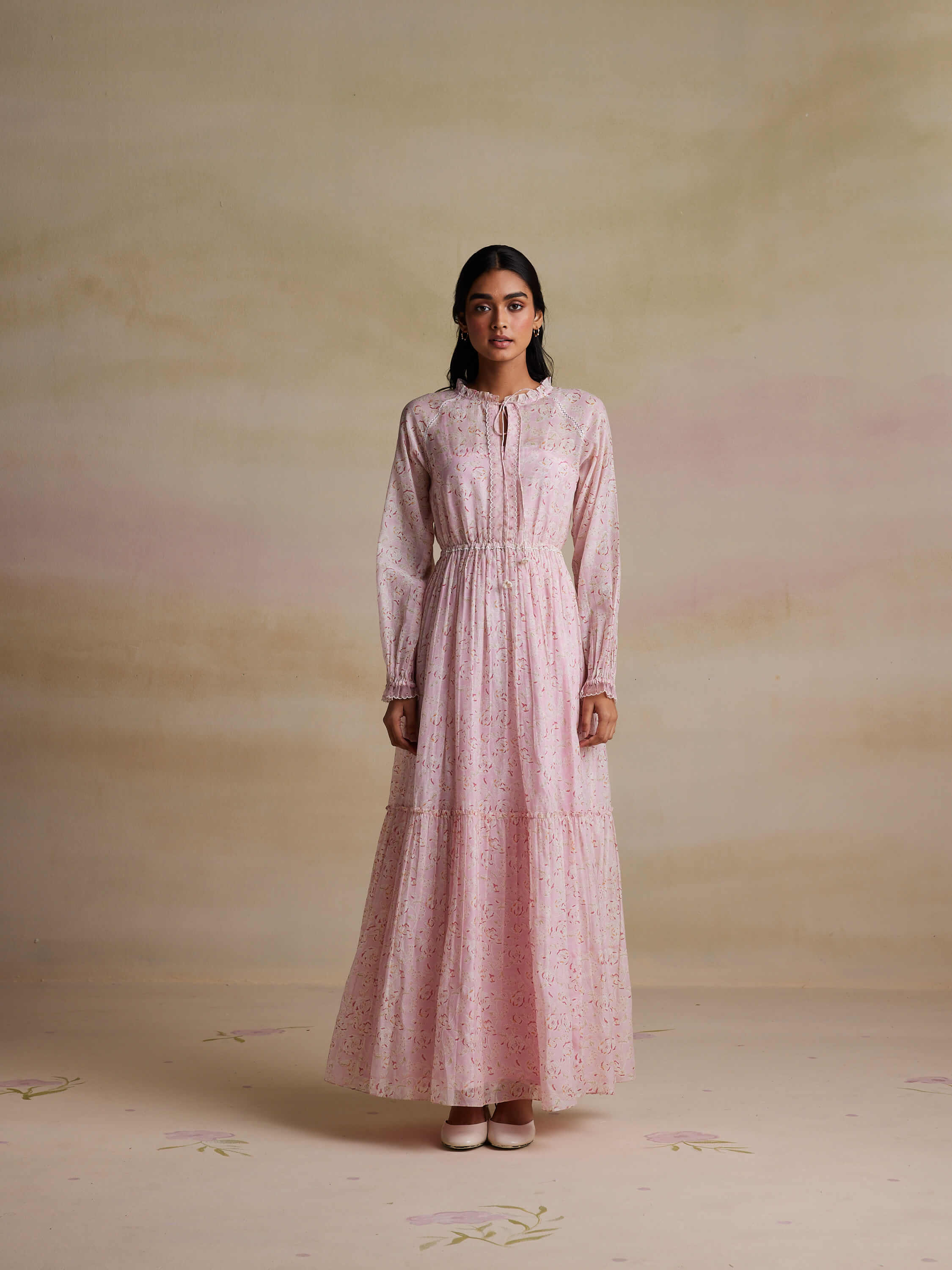 Woman wearing a long, pink floral dress standing indoors.