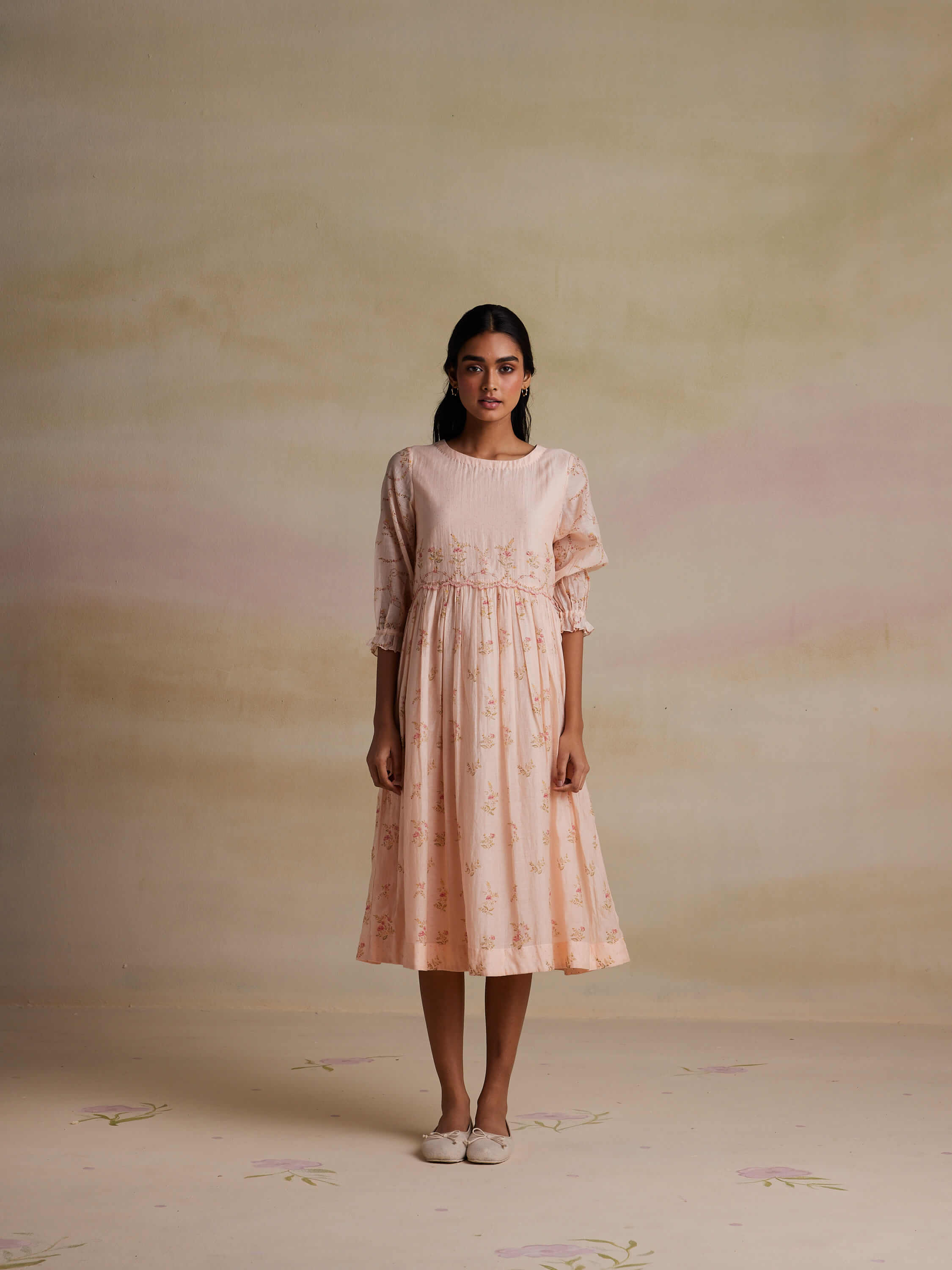 Woman in a pink floral dress posing against a muted background.