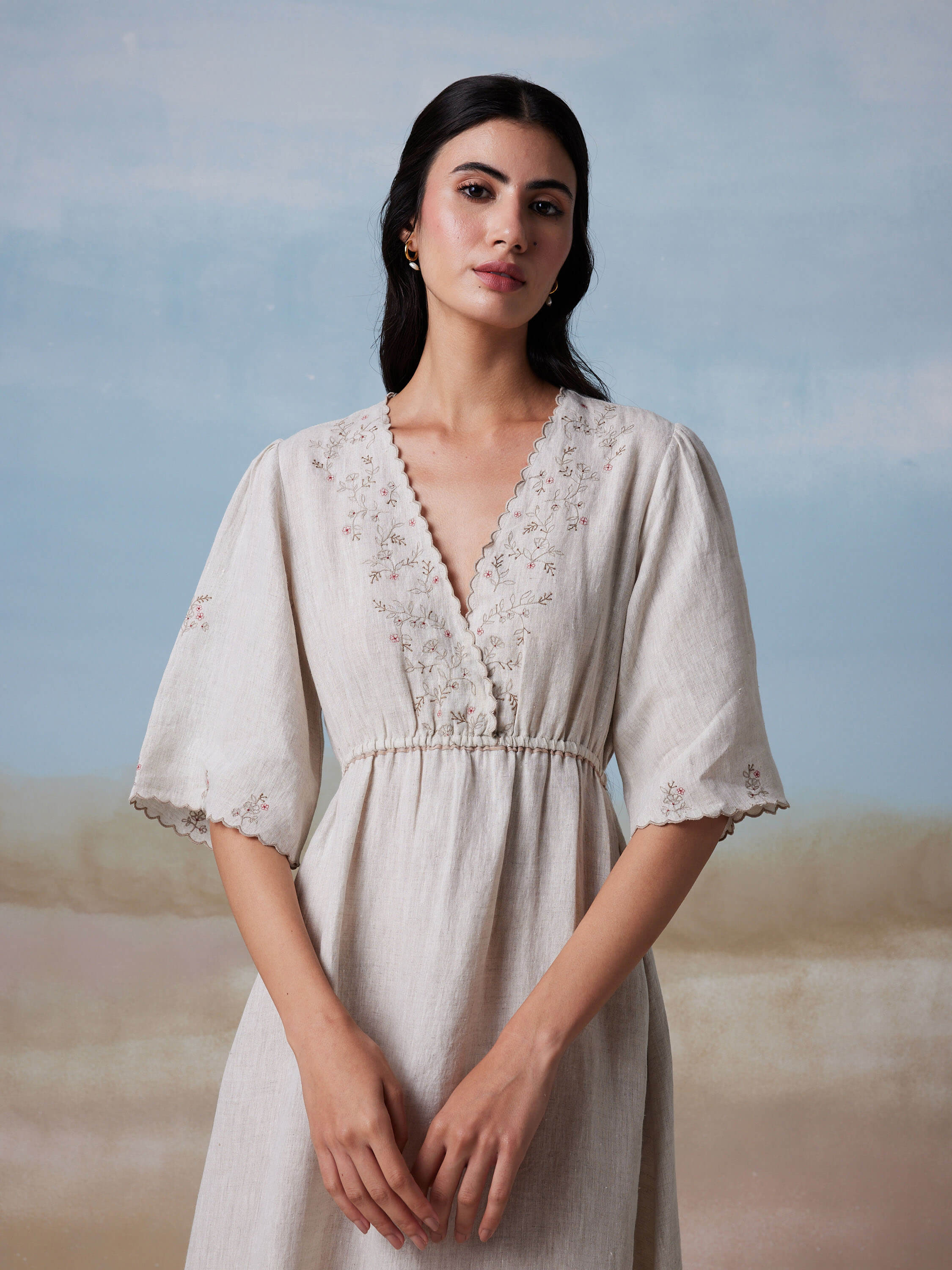 Woman in embroidered beige dress against a serene backdrop.