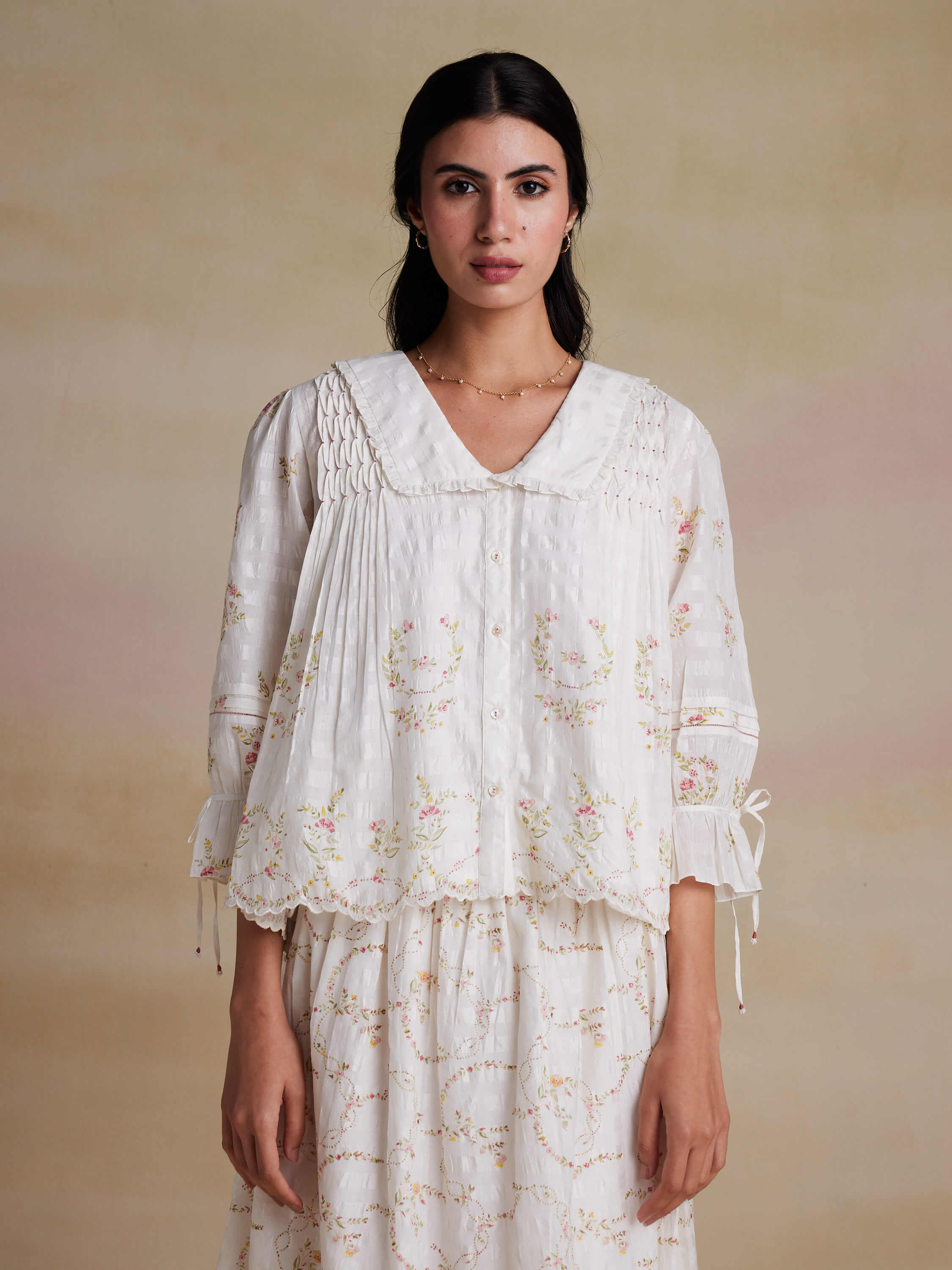 Woman wearing a white floral blouse and skirt, neutral background.