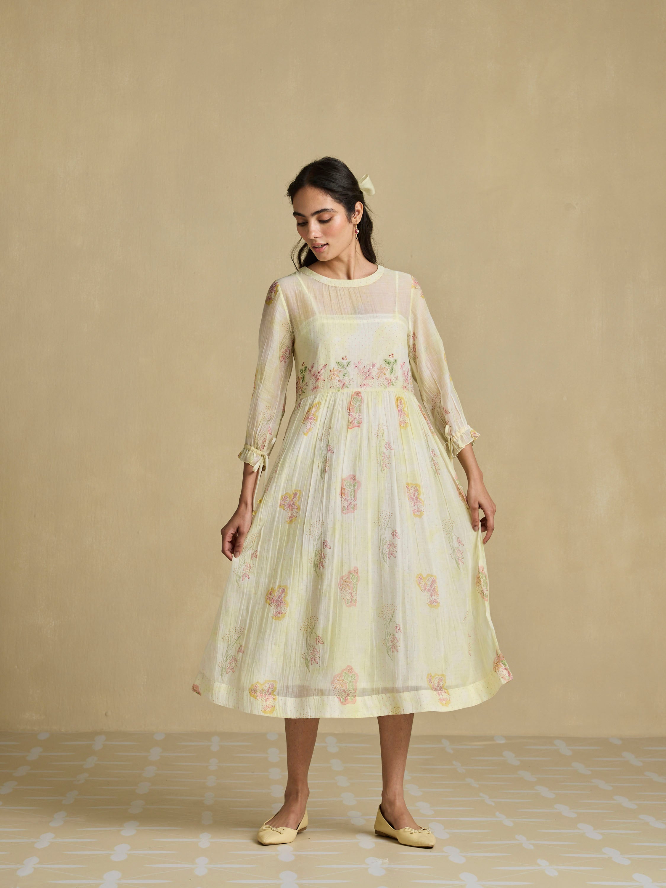 Woman wearing a light yellow floral dress against a beige background