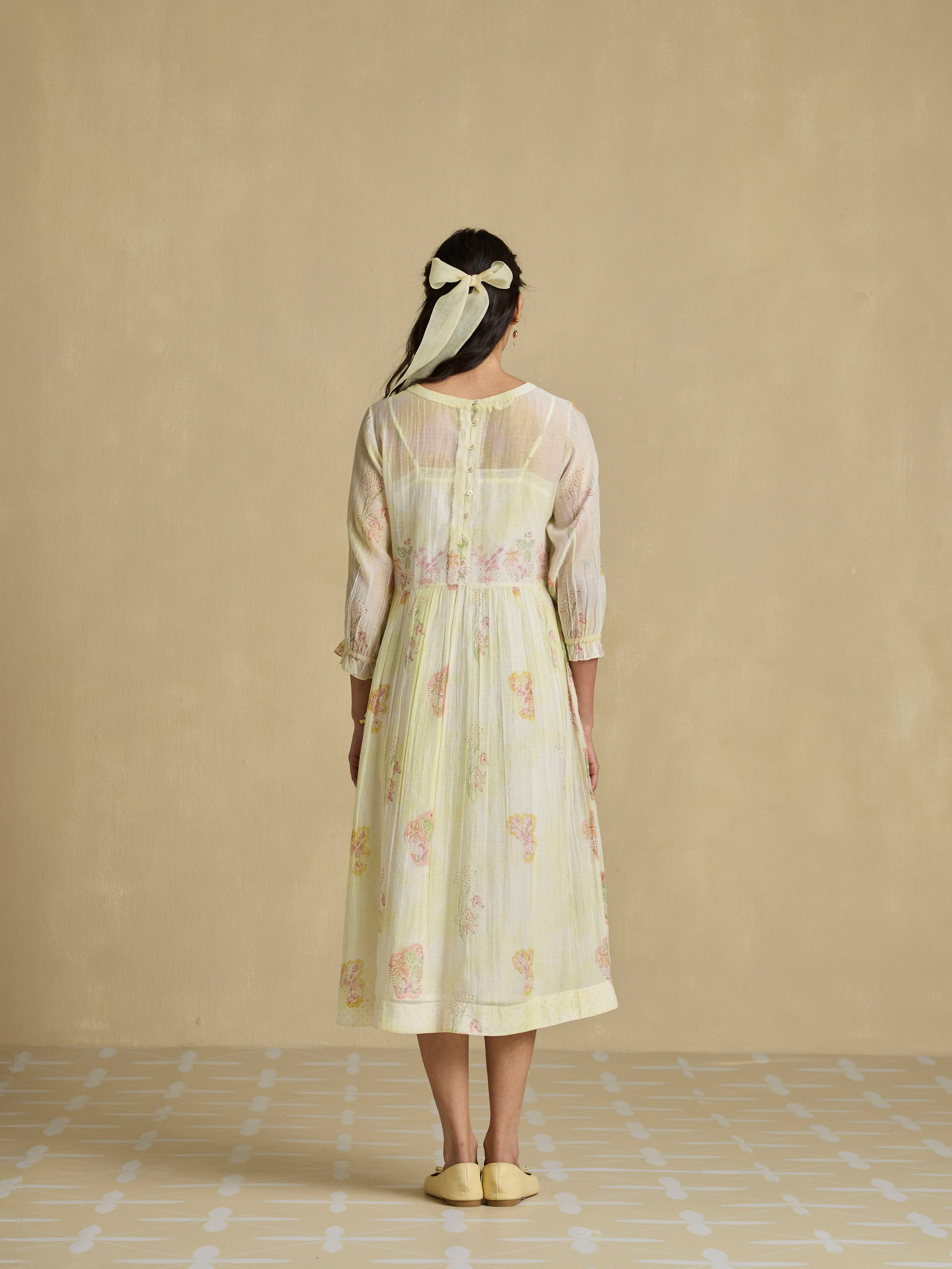 Woman wearing a light-colored dress with floral patterns against a beige background