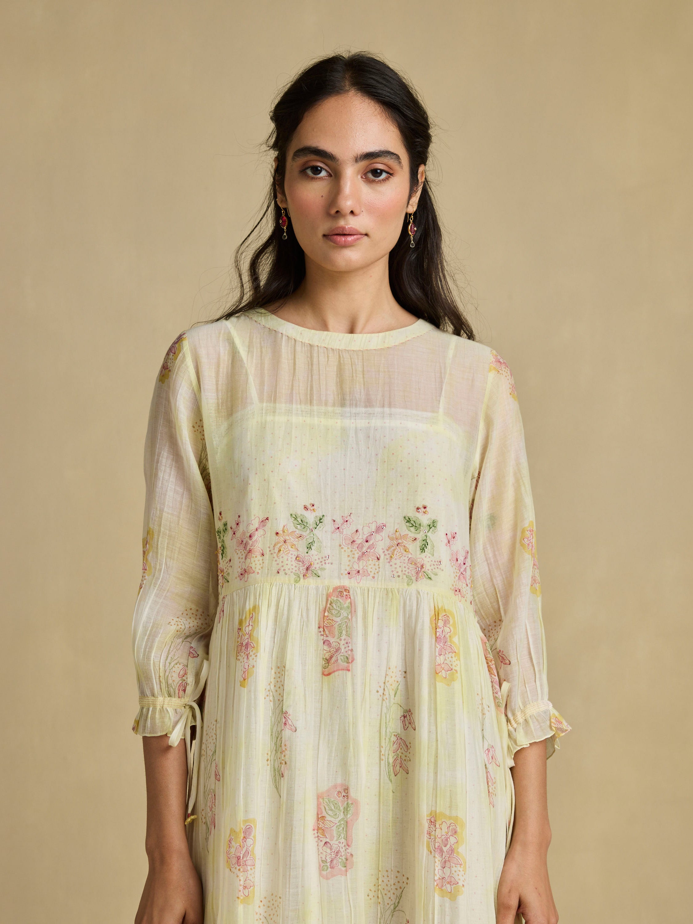 Woman wearing a light yellow floral dress against a beige background