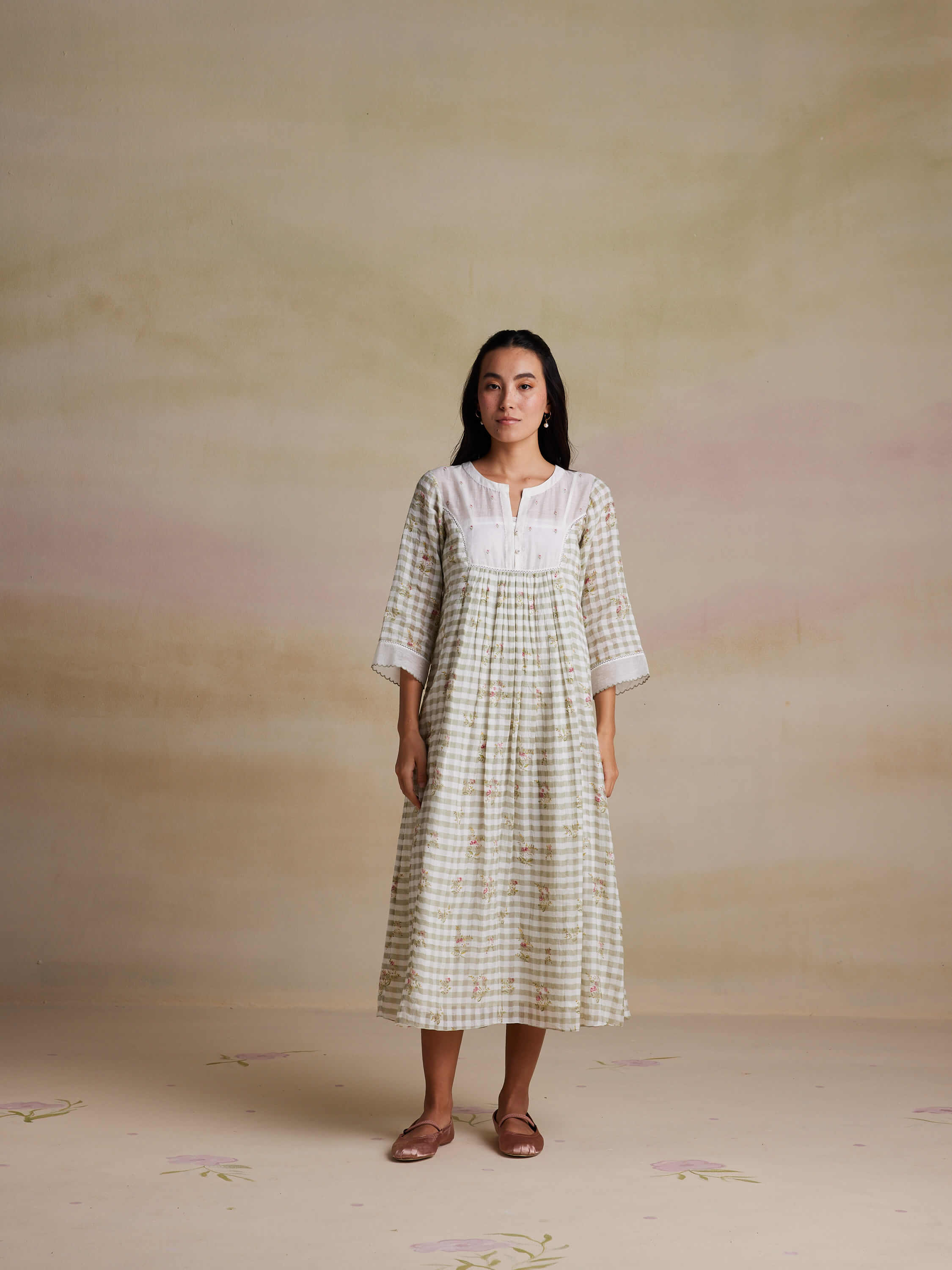 Woman in a checkered dress with floral print standing indoors.
