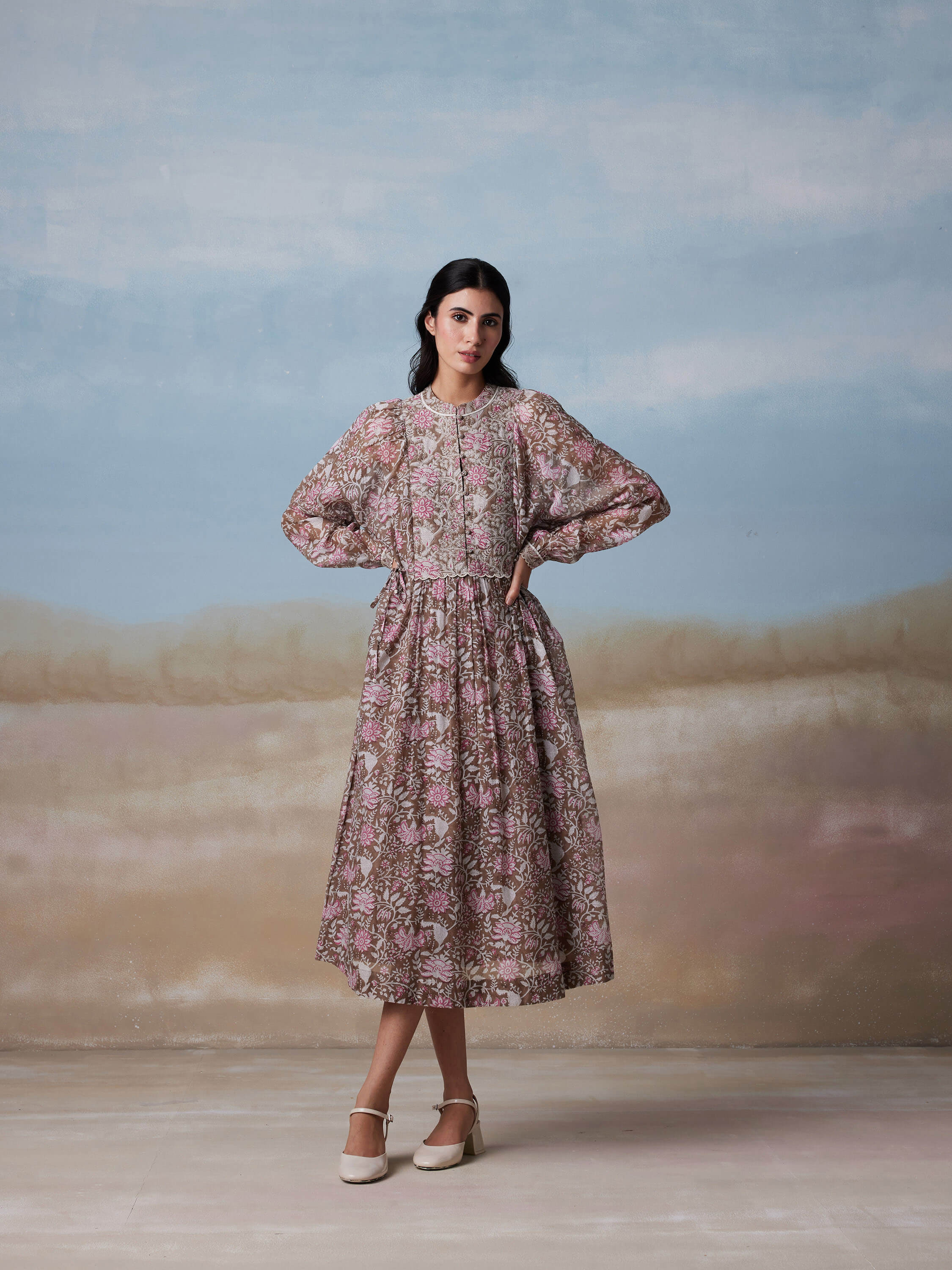 Woman wearing floral dress with puffy sleeves posing against a pastel background.